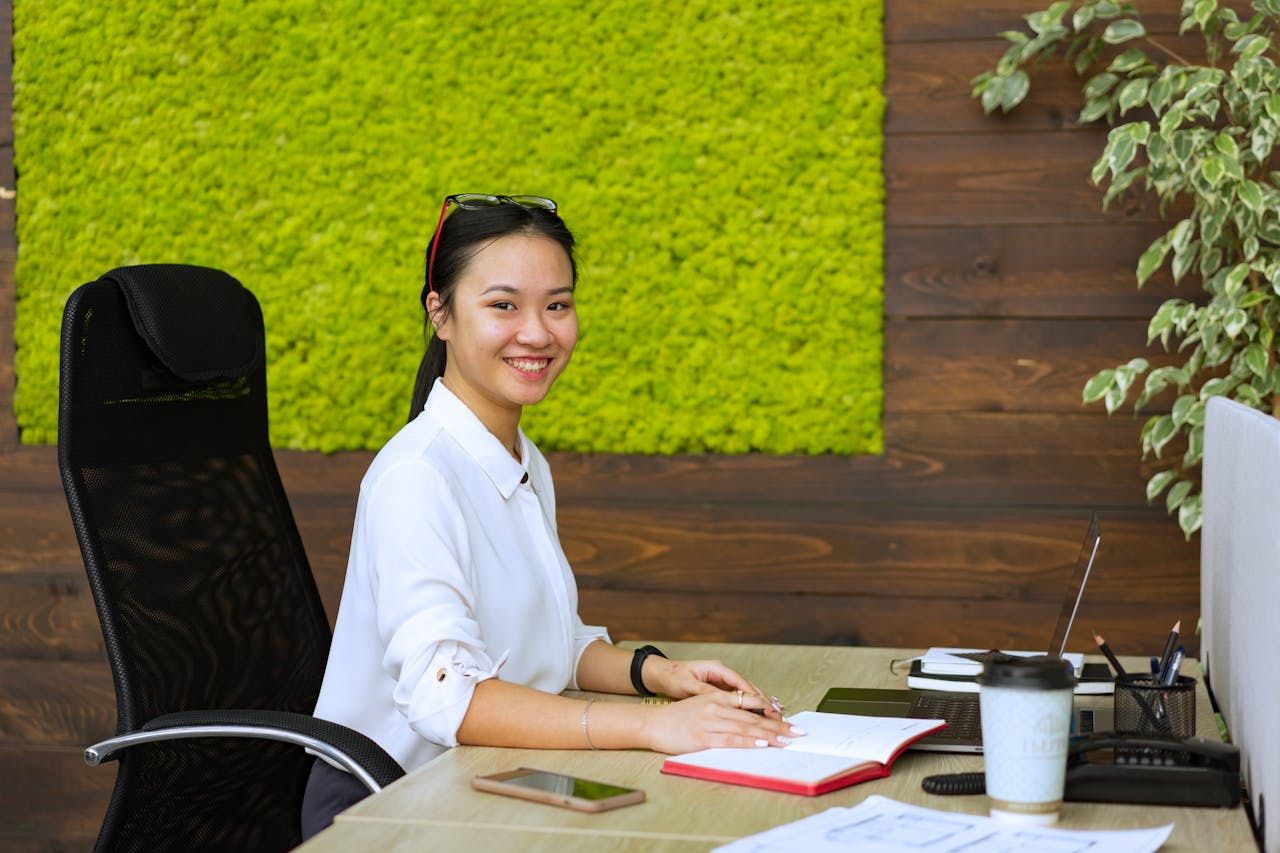 Young professional smiling at her desk with a notebook and laptop.