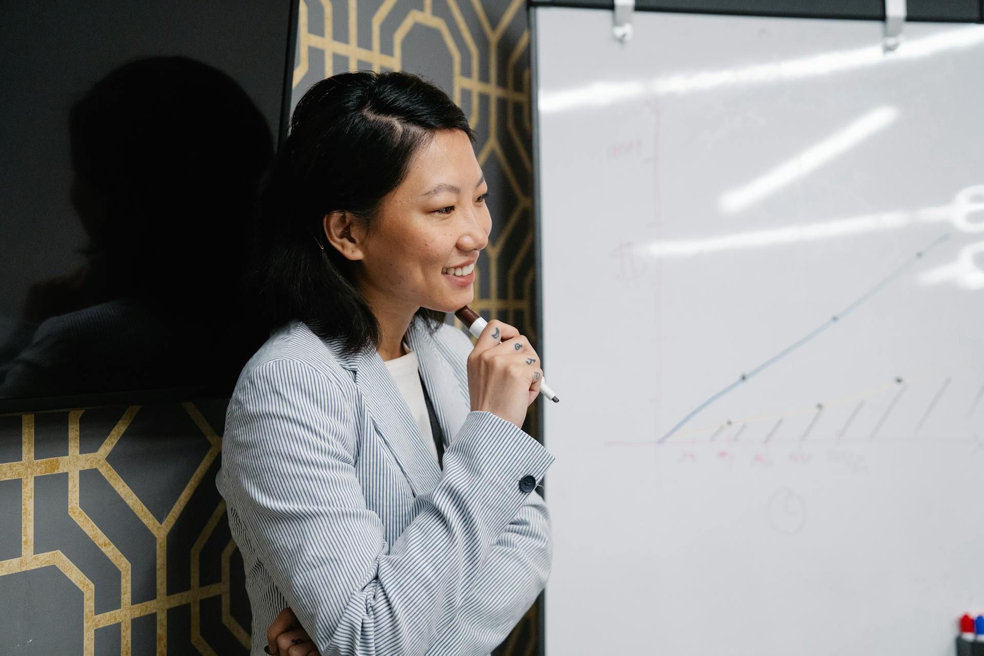 Woman presenting data trends on a whiteboard during a workplace meeting.