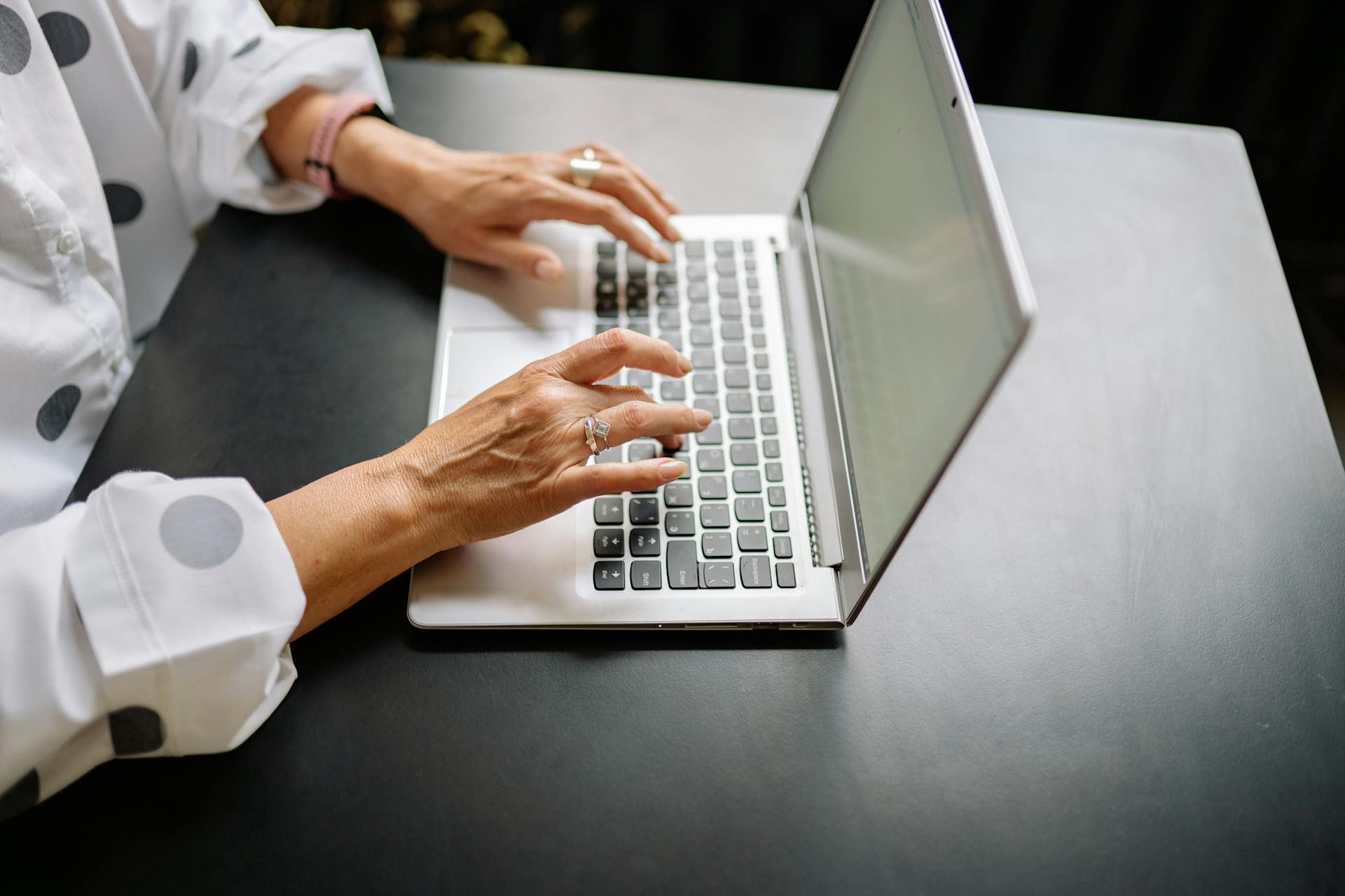 Close-up of a woman typing on a laptop keyboard at a desk.