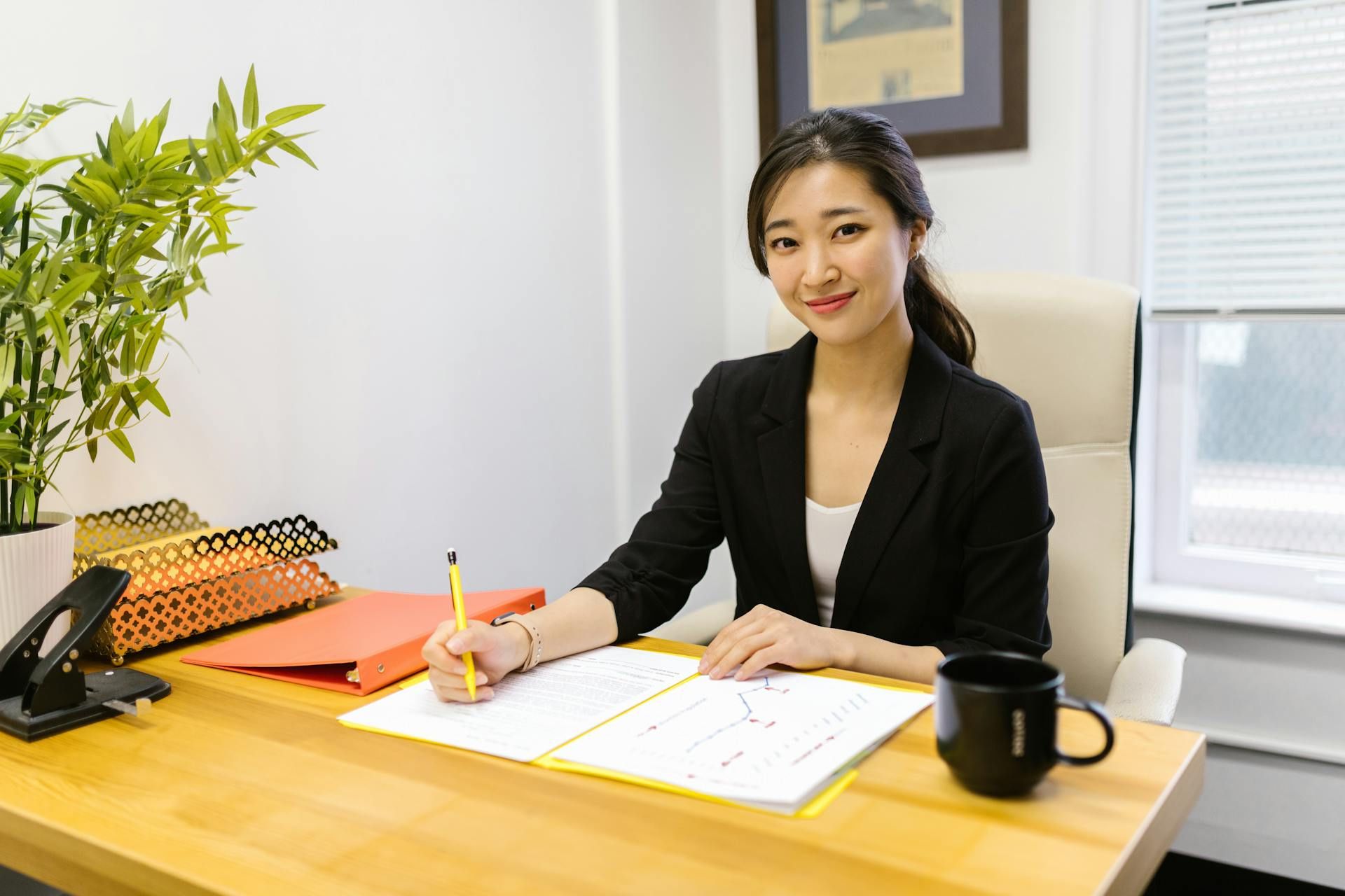 Professional woman smiling at her desk while reviewing documents and taking notes.