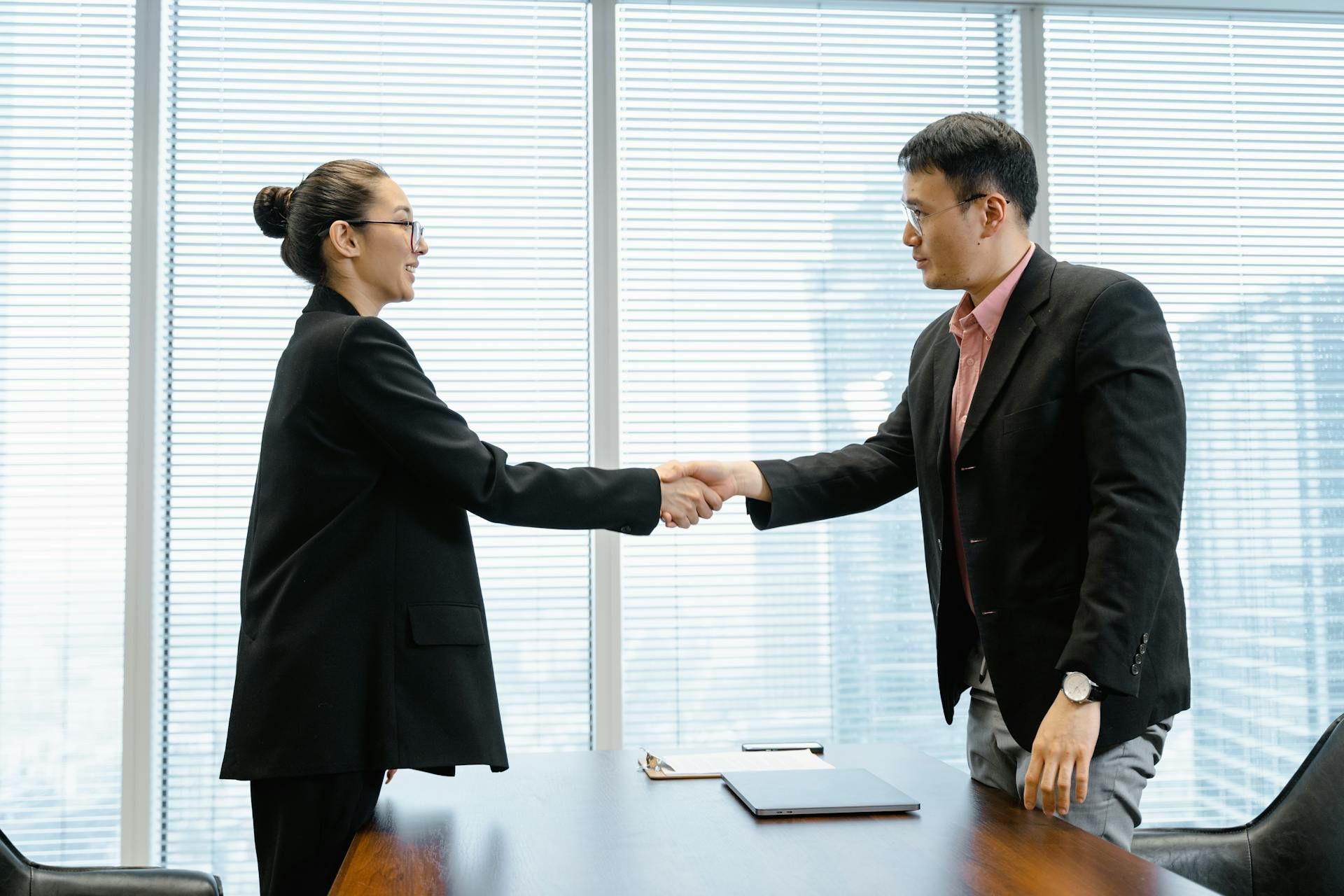 Two professionals shaking hands in a corporate office.