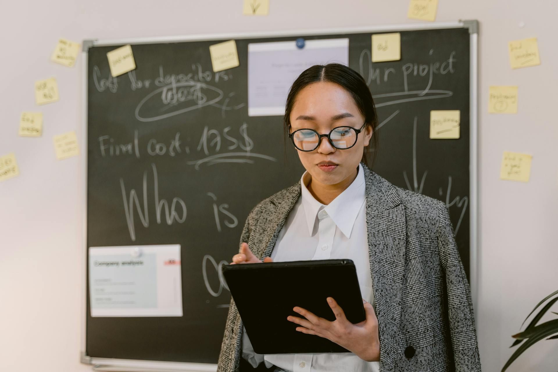 Seorang profesional perniagaan membaca maklumat pada tablet di hadapan papan perancangan projek.