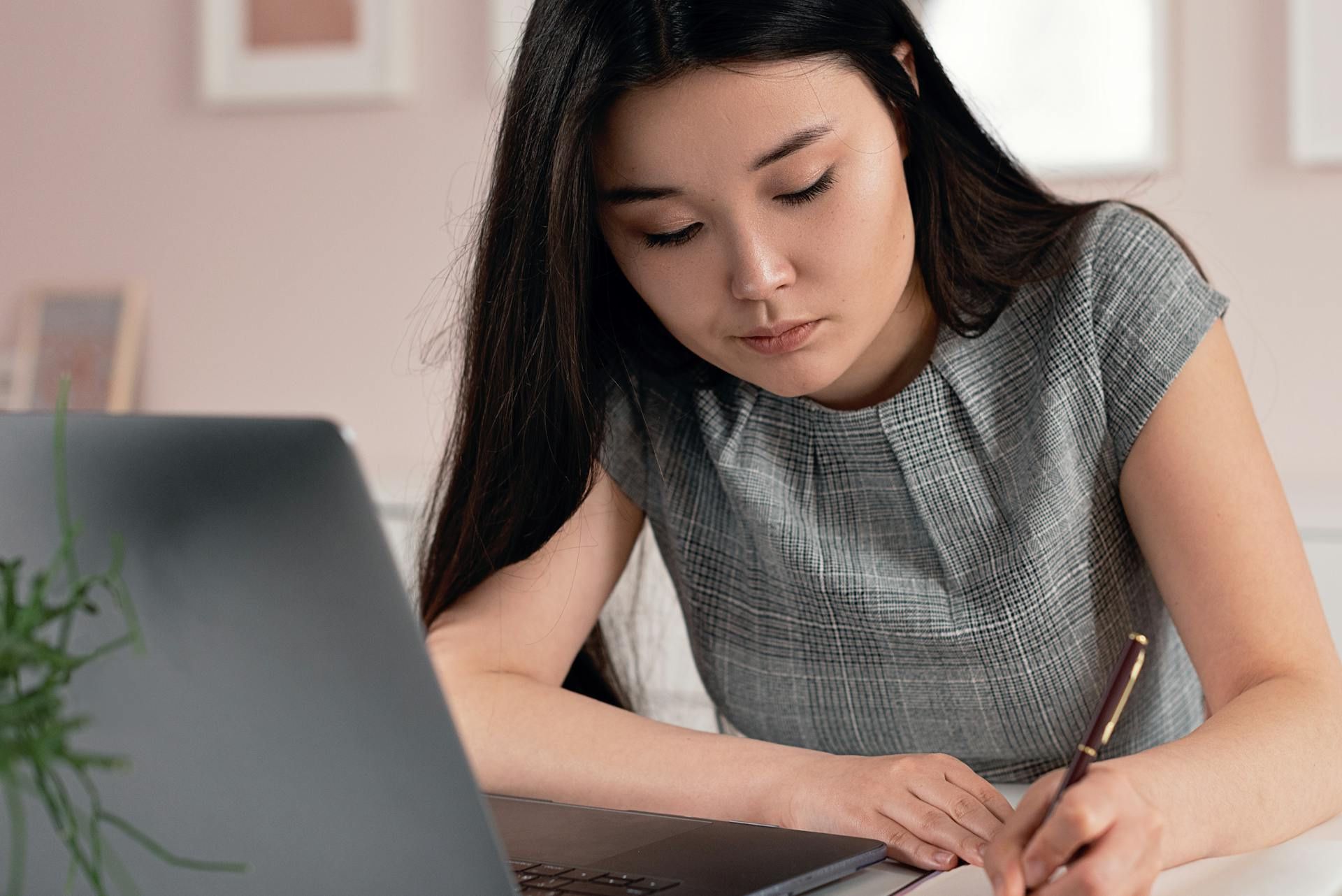 Young woman writing notes while working on a laptop at home. 