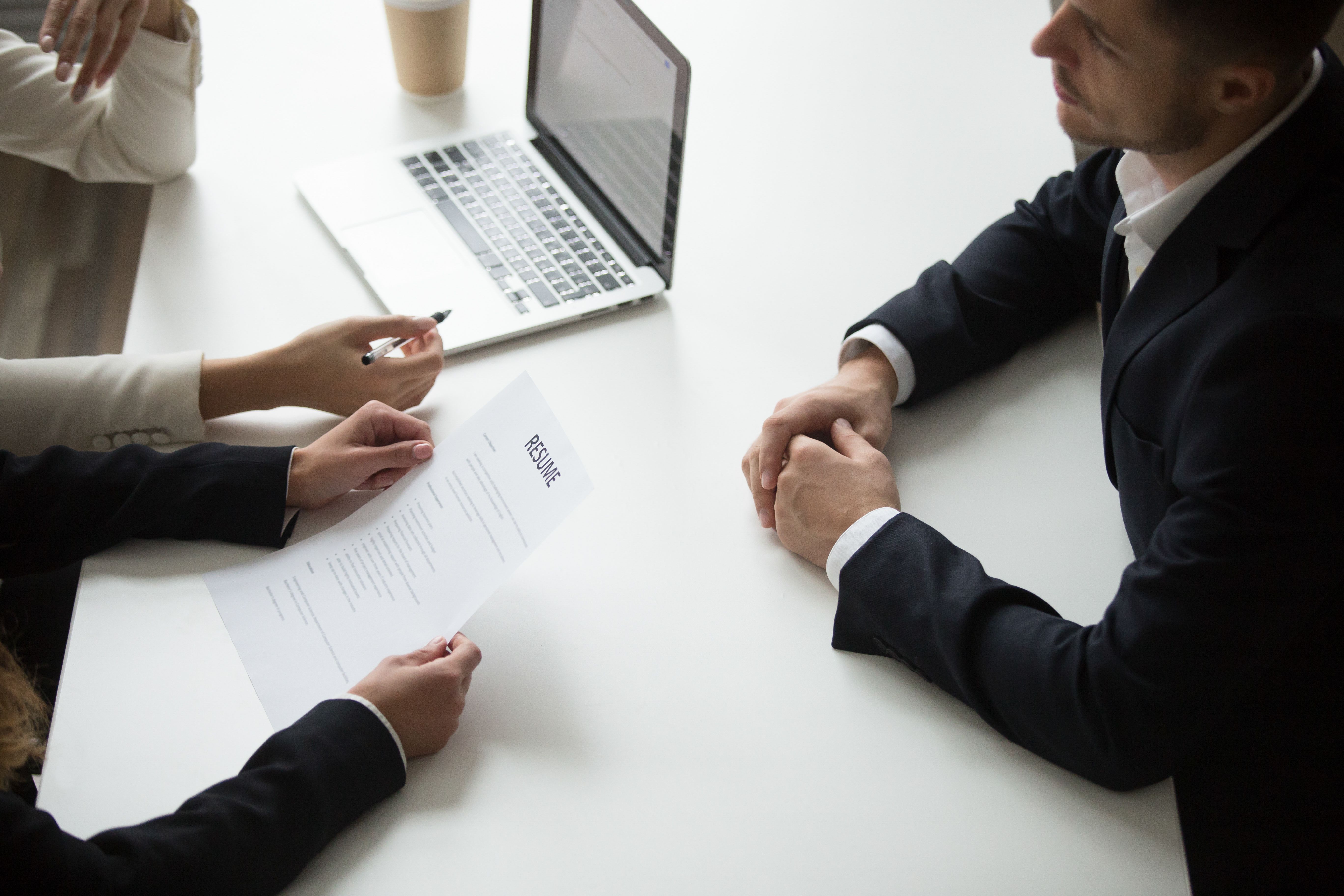 Close-up of a job interview with a candidate and two interviewers reviewing a resume; the image captures how positive leaders recognise successful efforts and potential during hiring decisions because of famous leadership quotes.
