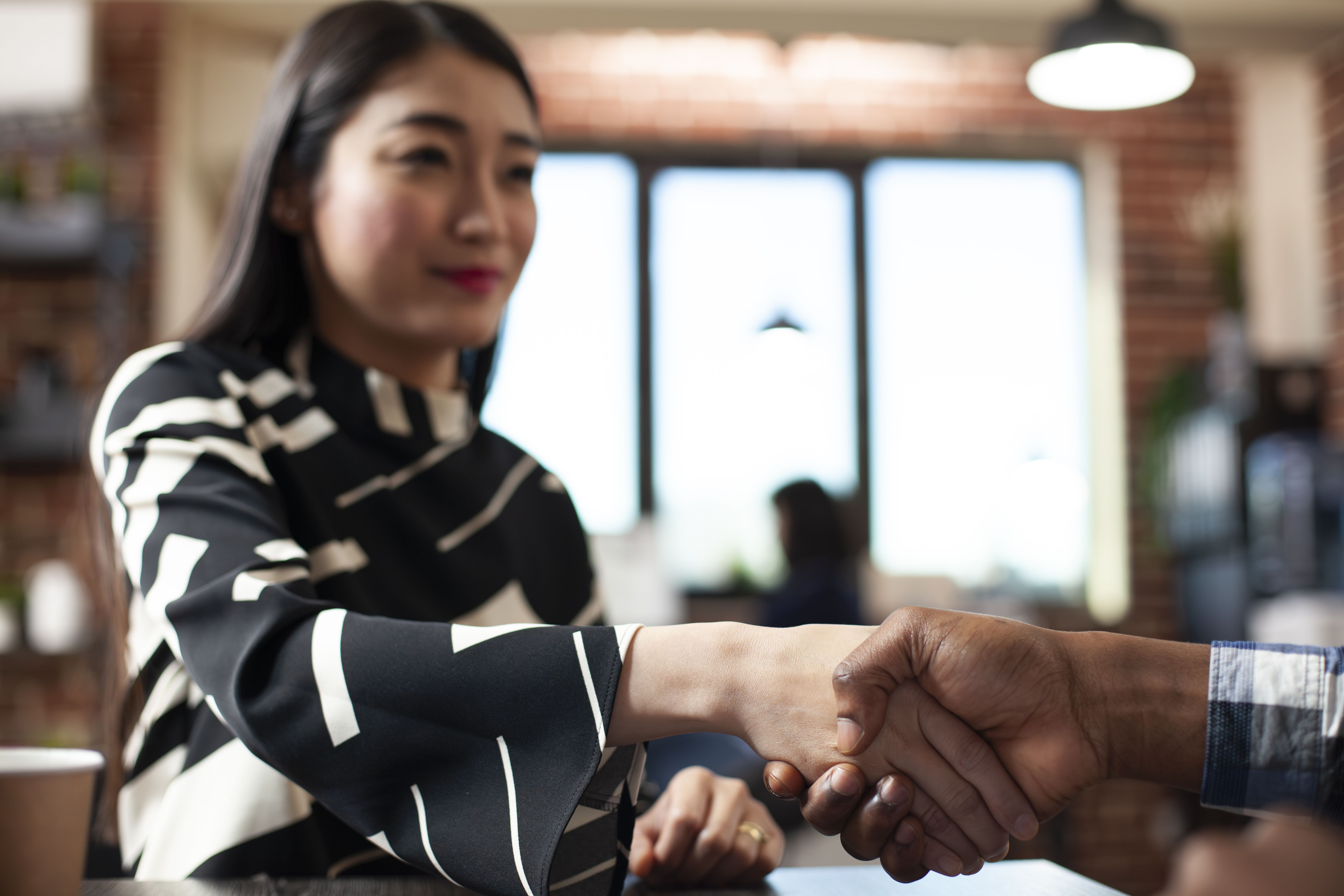 A woman in a black-and-white outfit shakes hands with another person. 