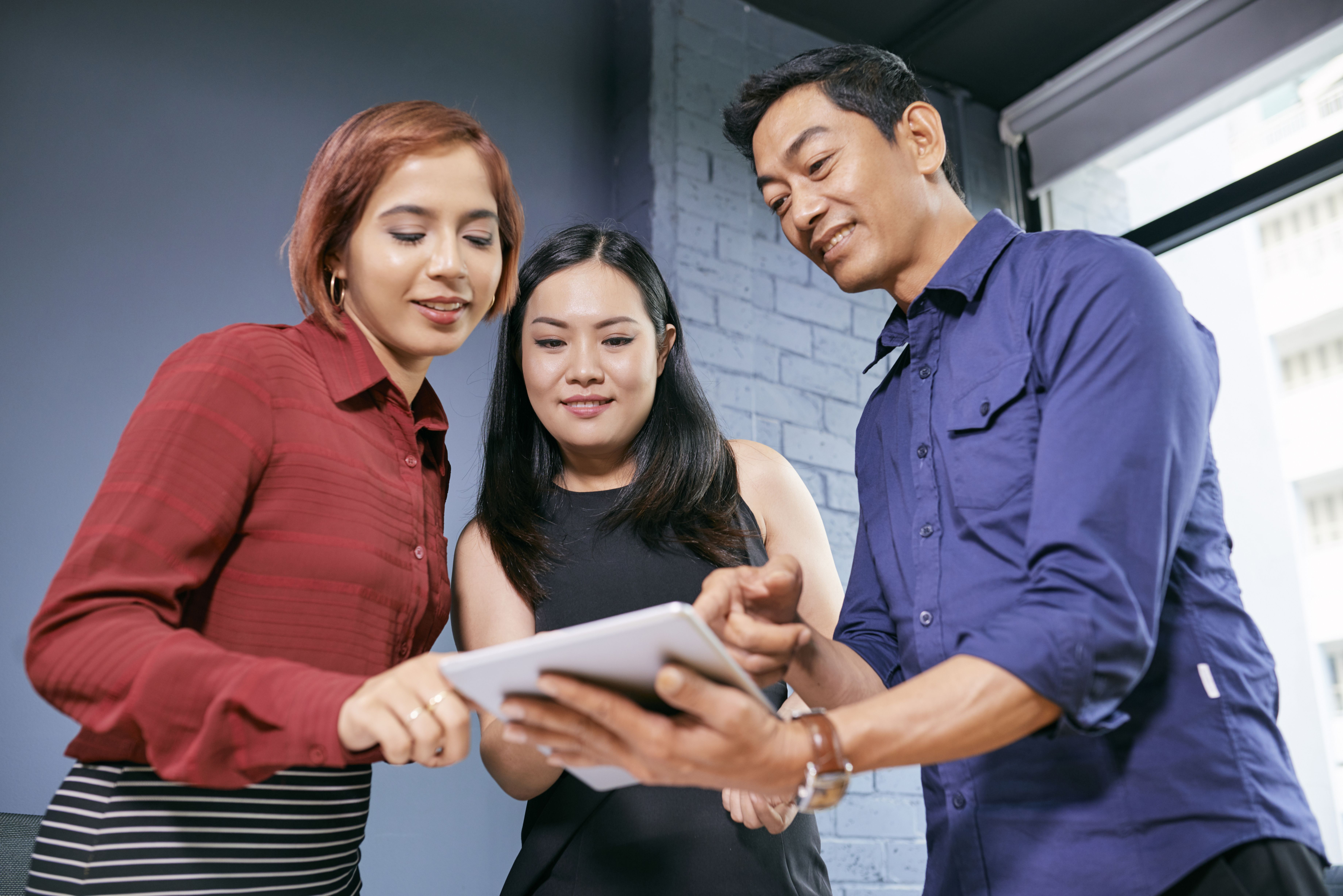 Three colleagues collaborating while reading leadership quotes from a tablet in a bright office; the image reflects how progress occurs when leaders instill a sense of shared purpose, openness, and teamwork.