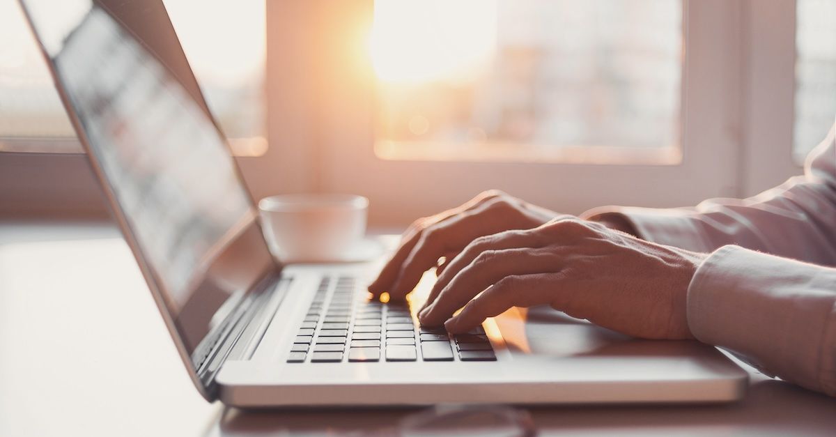Man typing on a laptop in the morning sunrise.