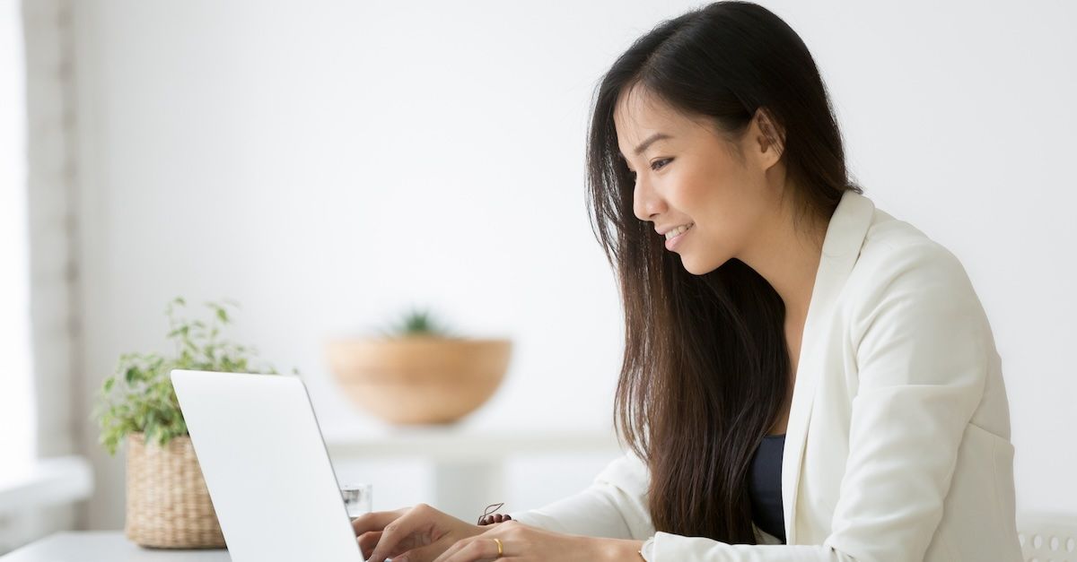 Woman in a white blazer typing on a laptop with a desk plant in the background