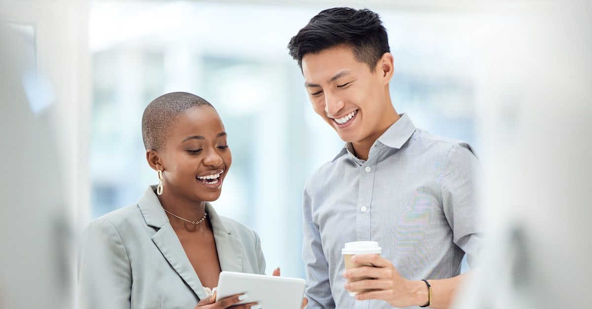 a man and woman talking and smiling while the woman holds a tablet and the man holds a cup of coffee