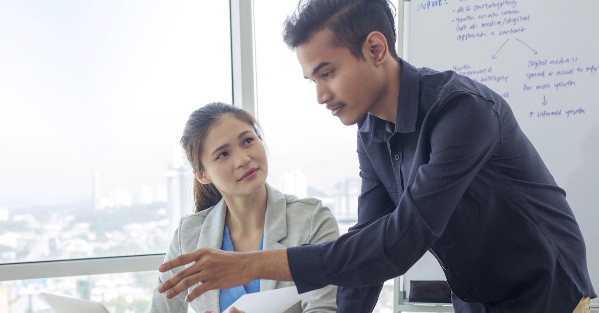 Man in a blue shirt talking to a woman at her desk during a performance review