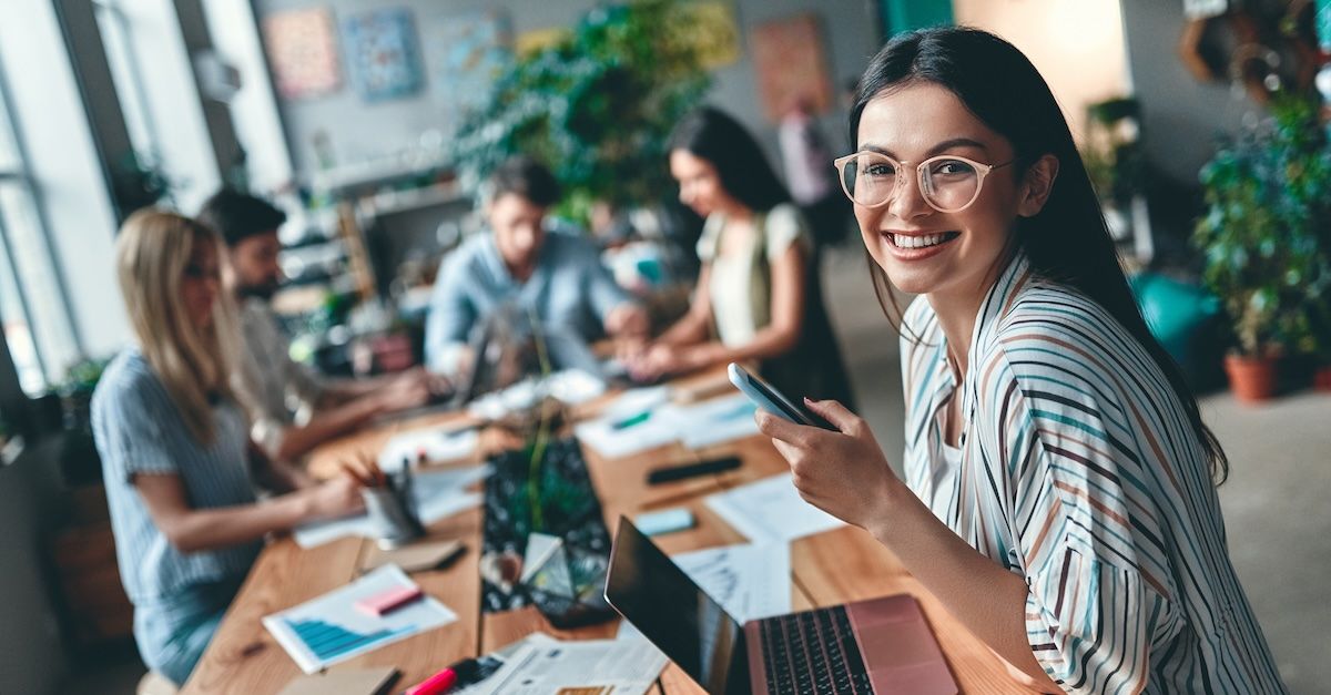 Woman at work table with coworkers behind her