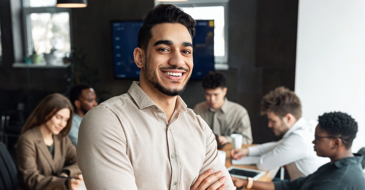 Man in a tan shirt smiling in front of a work team