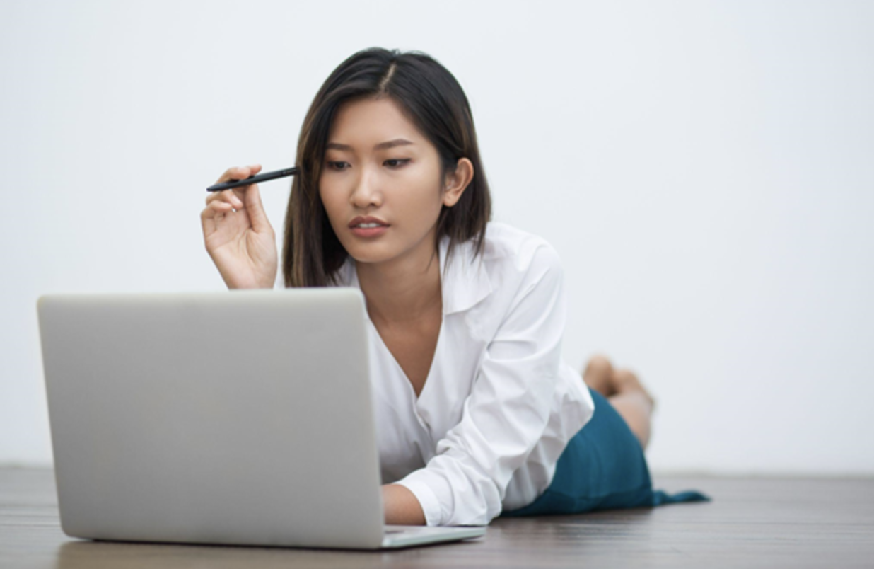Woman in a white shirt and blue skirt lying on floor using a laptop
