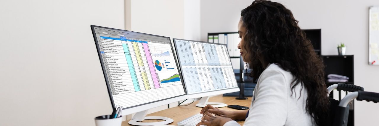 Woman working on spreadshets at a desk with two monitors
