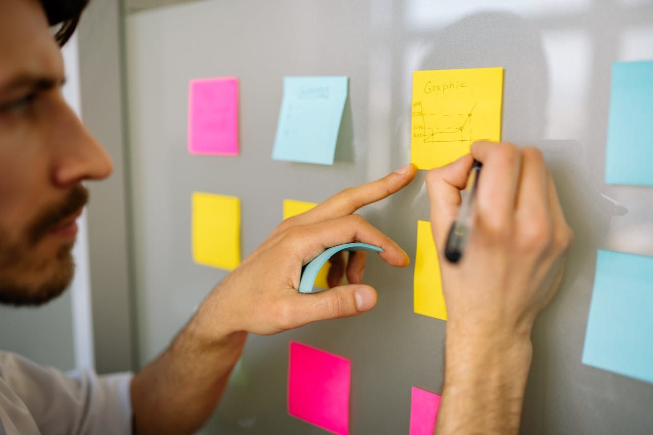 Seorang lelaki mencatat cadangan projek pada nota melekat semasa sesi brainstorming idea.