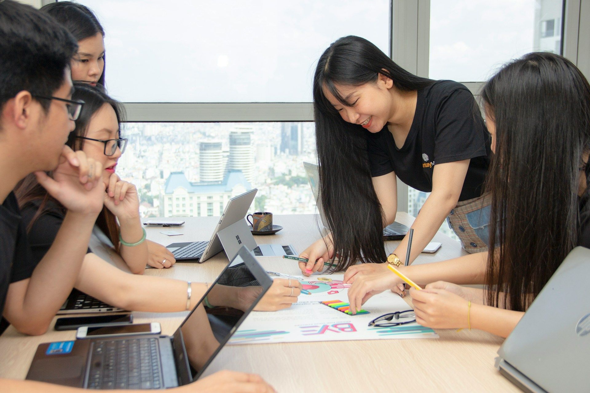 Beberapa individu berkerja secara berkumpulan di pejabat, berkongsi idea dan berkolaborasi dengan peralatan digital untuk menyelesaikan tugas, menggambarkan pengurusan projek yang efektif.