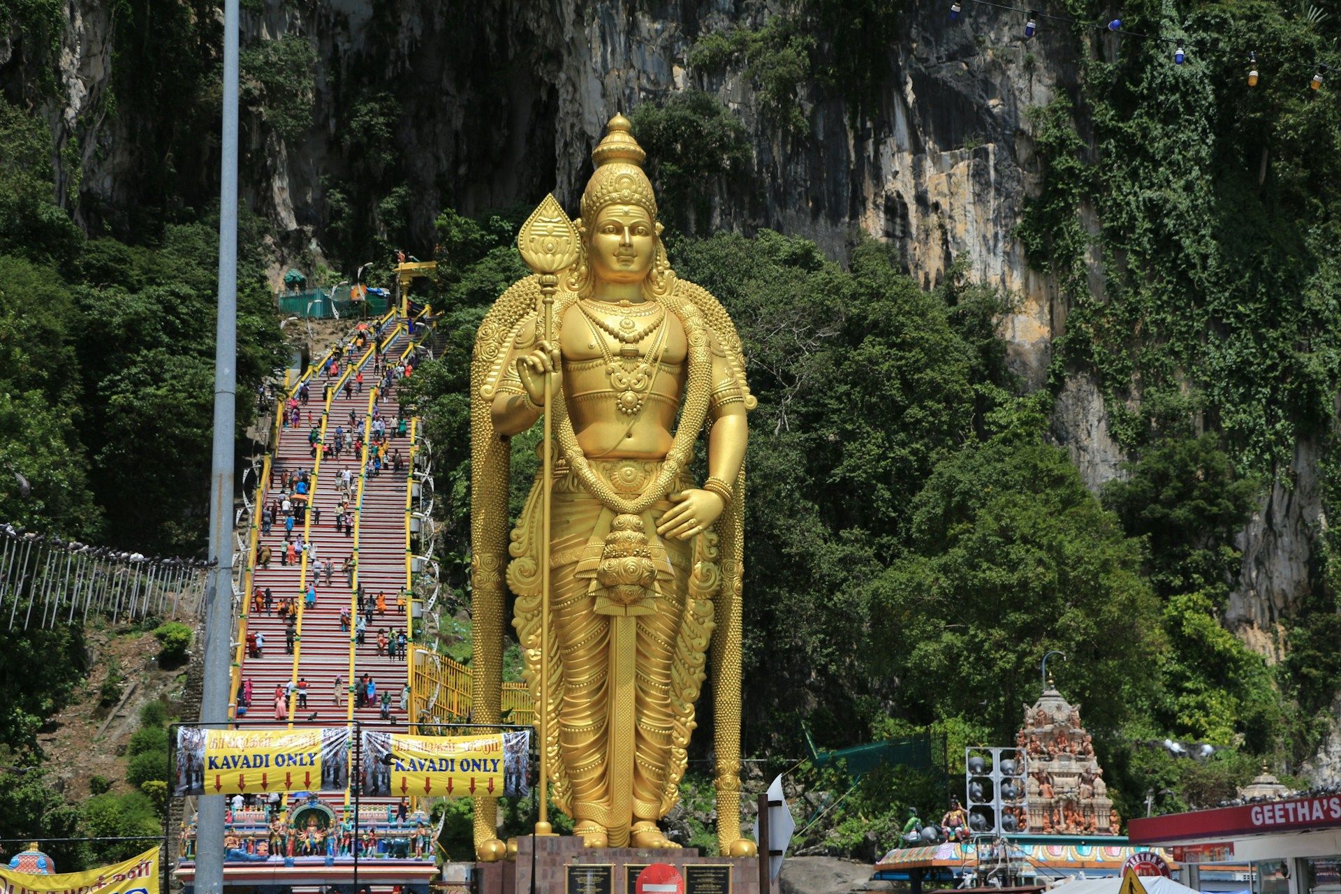 Patung emas besar Dewa Murugan di Batu Caves, dengan orang ramai mendaki tangga sempena sambutan Thaipusam.