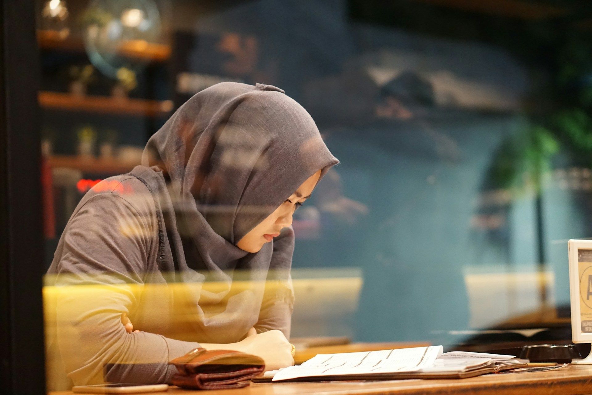 Seorang wanita memakai tudung sedang membaca sehelai kertas.