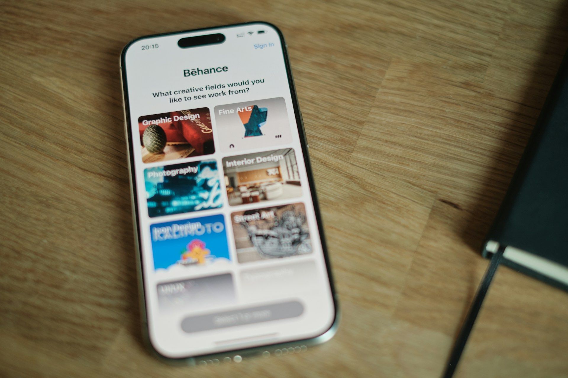Paparan platform Behance di telefon pintar yang memaparkan kategori portfolio kreatif seperti reka bentuk grafik dan fotografi.