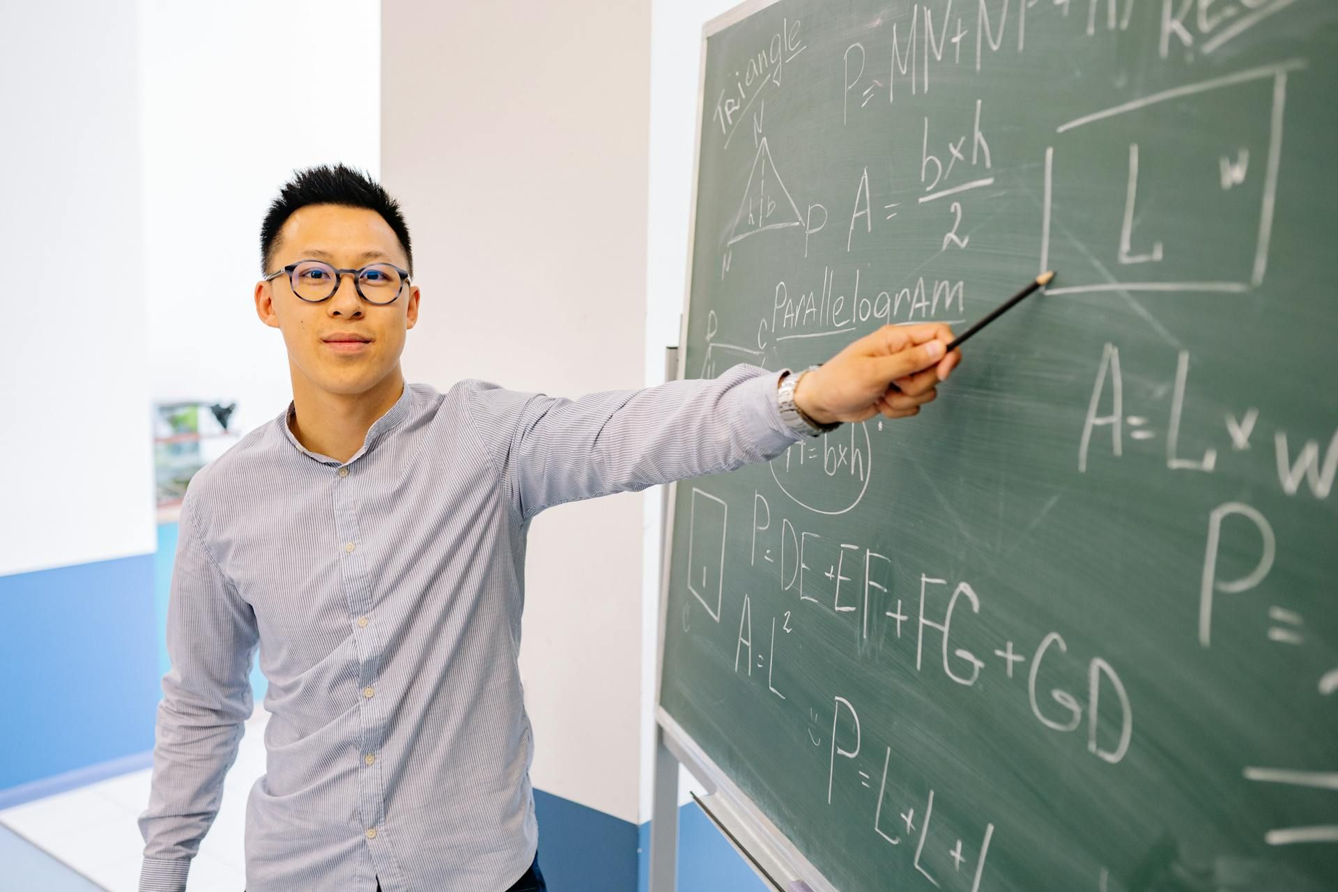 Guru lelaki mengajar subjek Matematik menggunakan papan hitam dalam suasana kelas sekolah menengah.