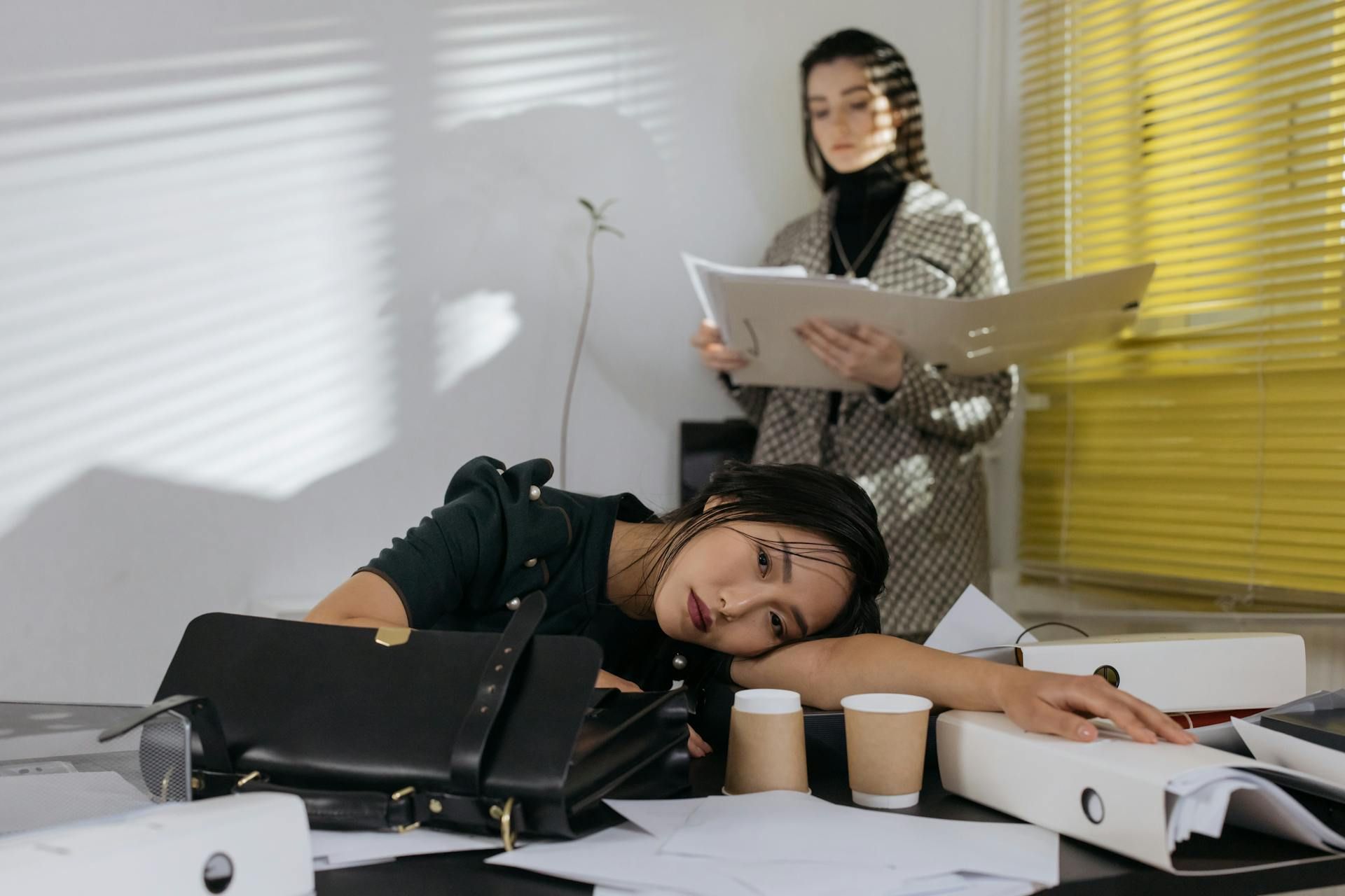 Pekerja keletihan di meja kerja dengan dokumen berselerak, menunjukkan tekanan dan kehilangan motivasi.
