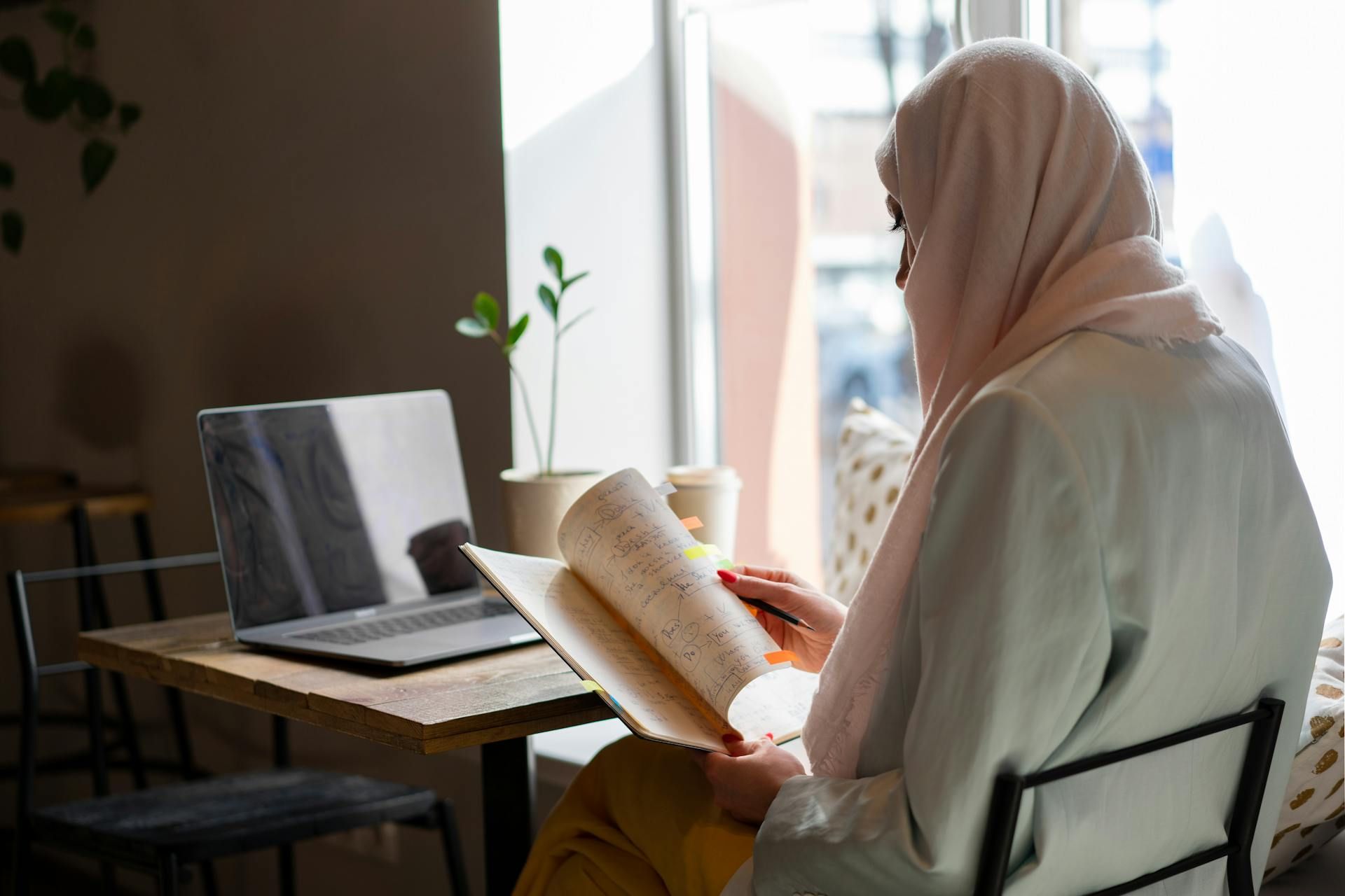 Seorang wanita bertudung sedang membaca buku notanya.