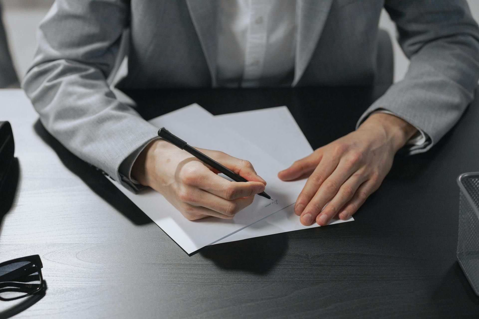 Individu menulis surat berhenti kerja secara profesional di atas meja hitam.