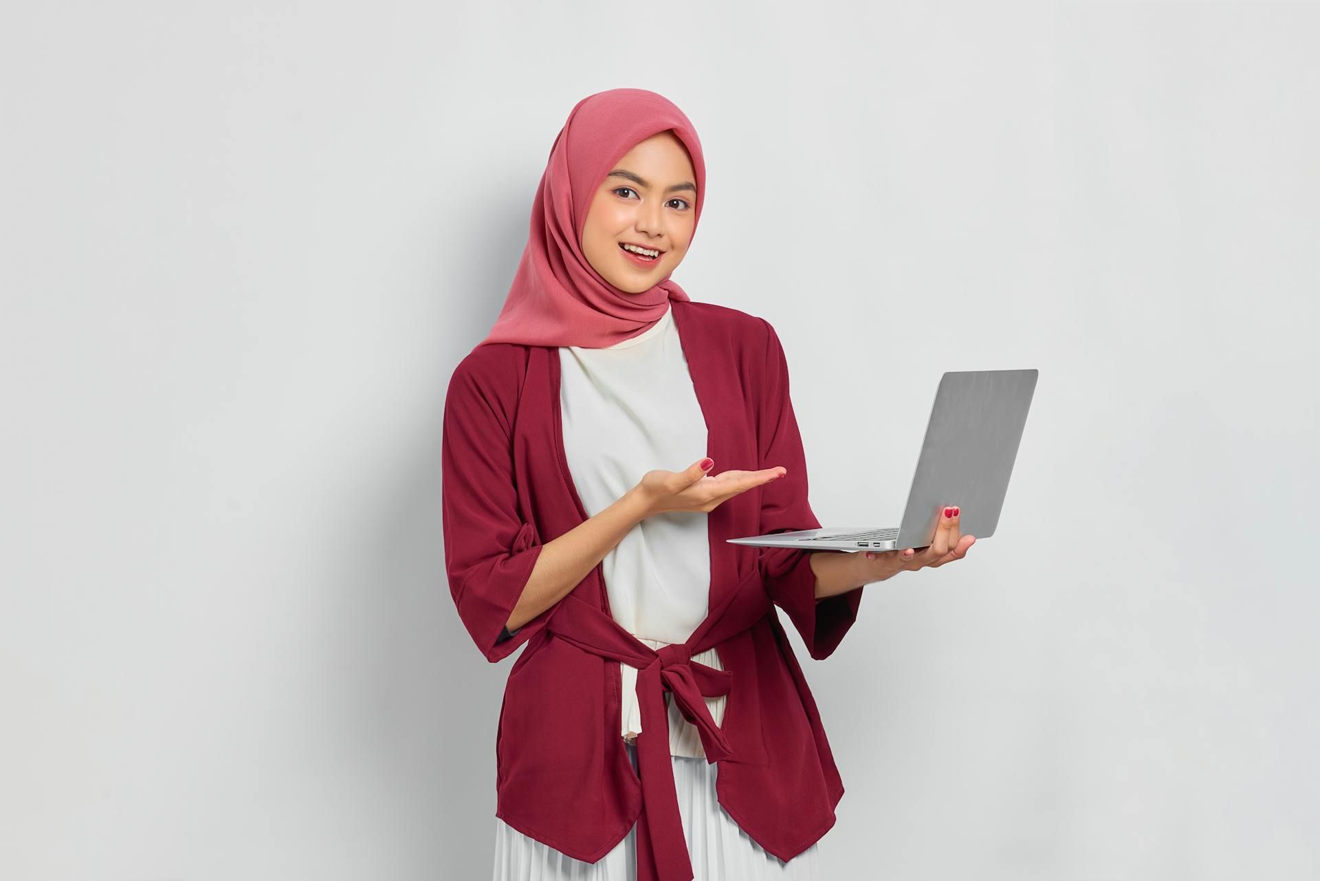 Seorang wanita memakai tudung sedang memegang komputer ribanya.