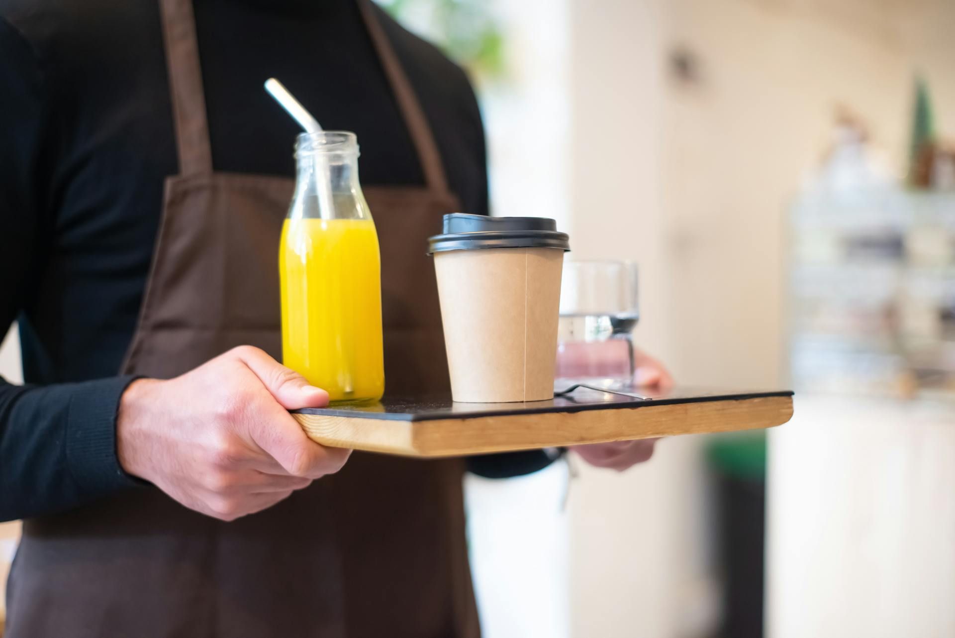 Pekerja restoran sedang membawa dulang berisi jus oren dan kopi.