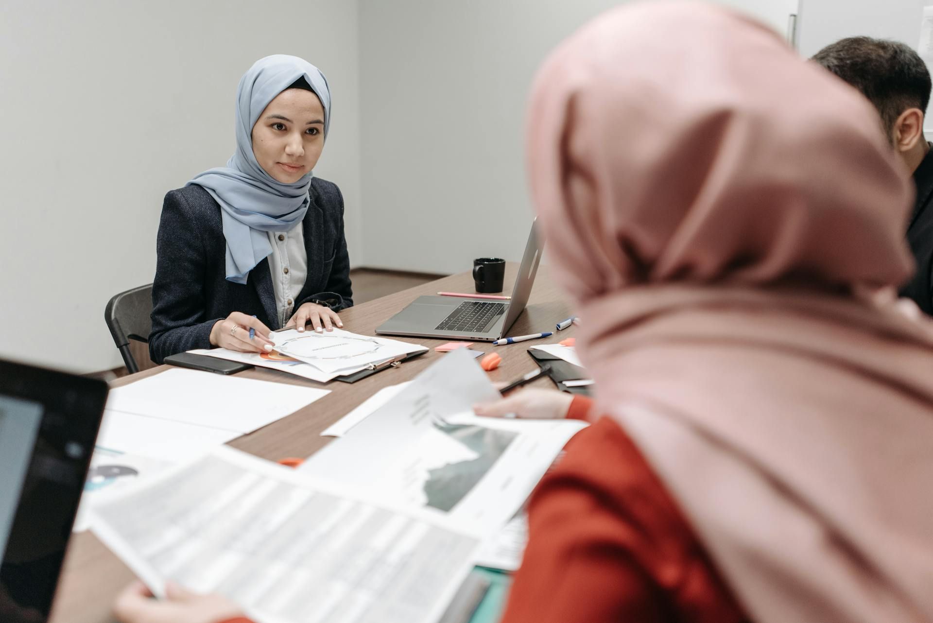 Dua orang wanita berhijab sedang berbincang tentang kerja di pejabat.
