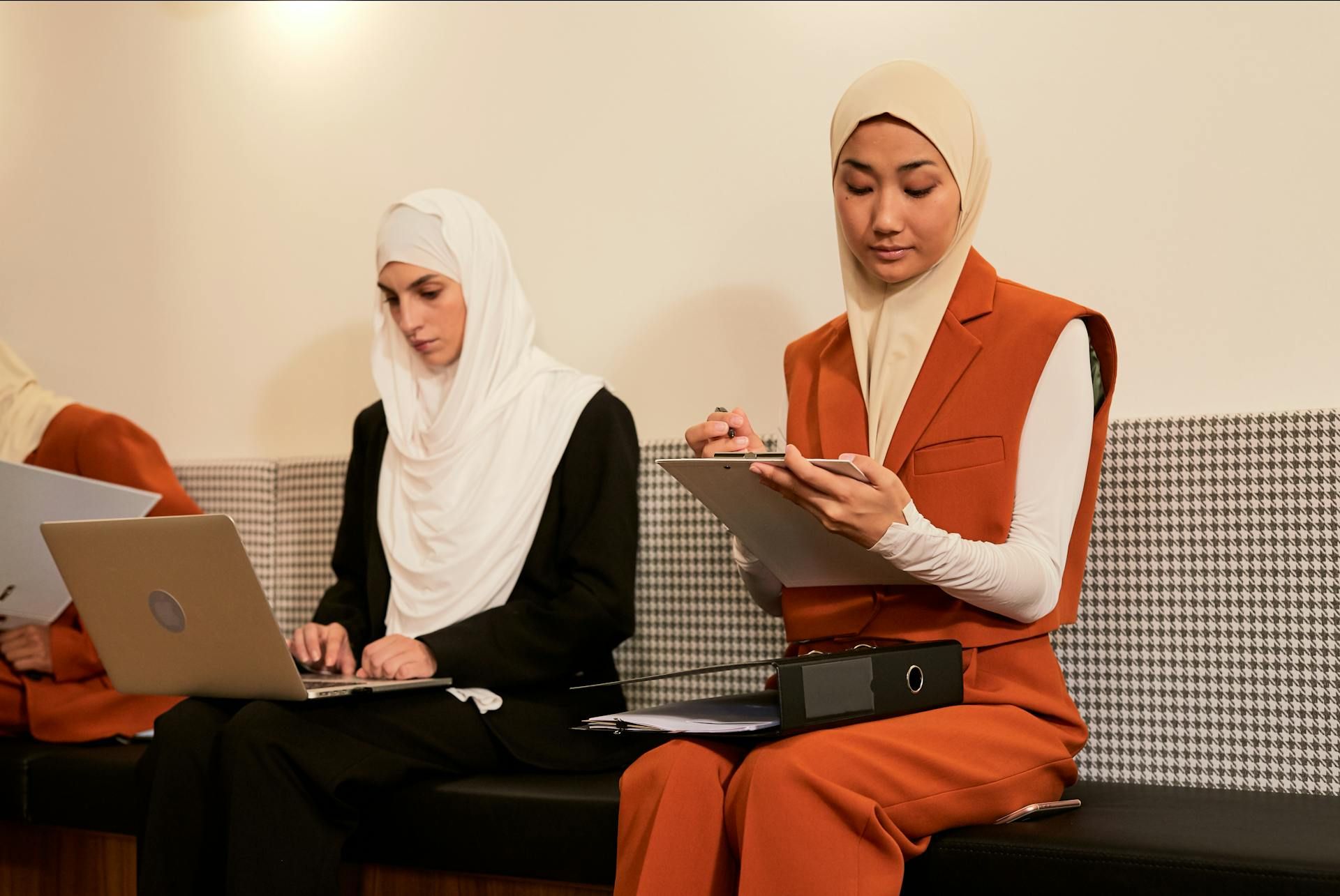 Dua orang wanita berhijab sedang bekerja sambil duduk.