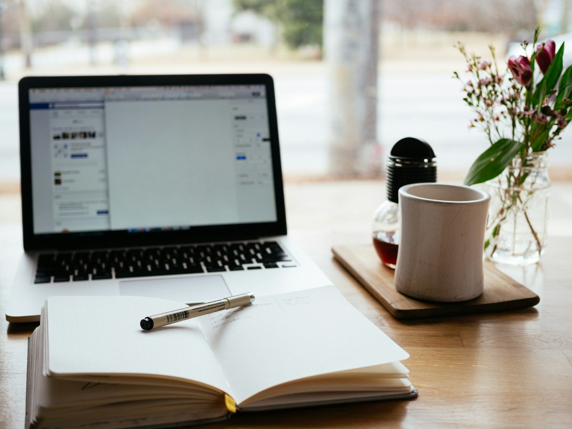 Meja kerja dengan komputer riba, buku nota dan cawan kopi yang digunakan untuk menyusun portfolio kerja digital.