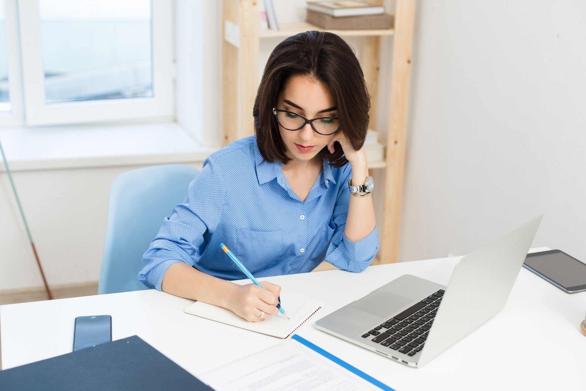 A woman drafting an application letter in a notebook beside a laptop while preparing for a job application in Malaysia. 