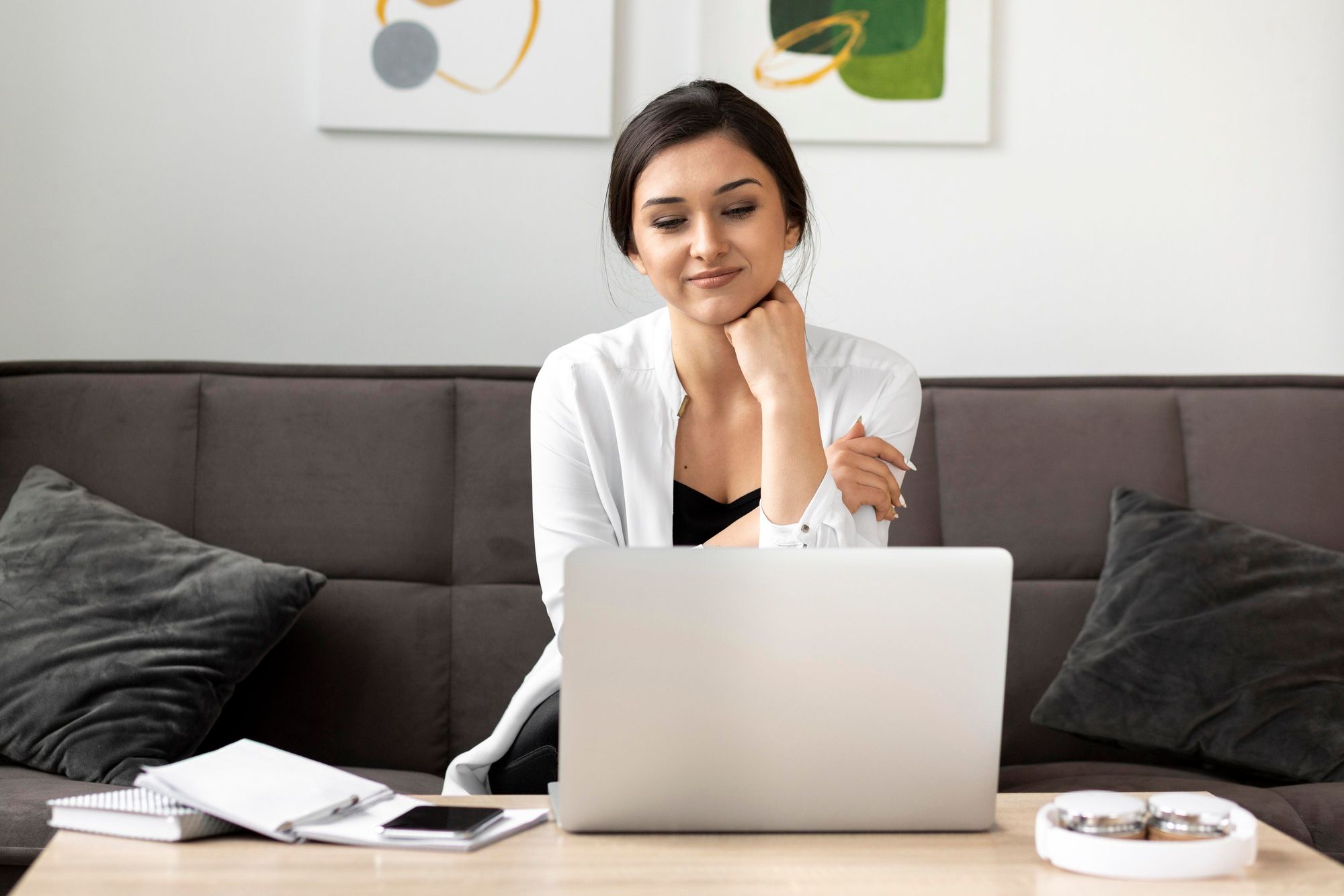 Woman sitting on a sofa, reading resume summaries. A notebook, smartphone, and other items are on the coffee table in front of her.