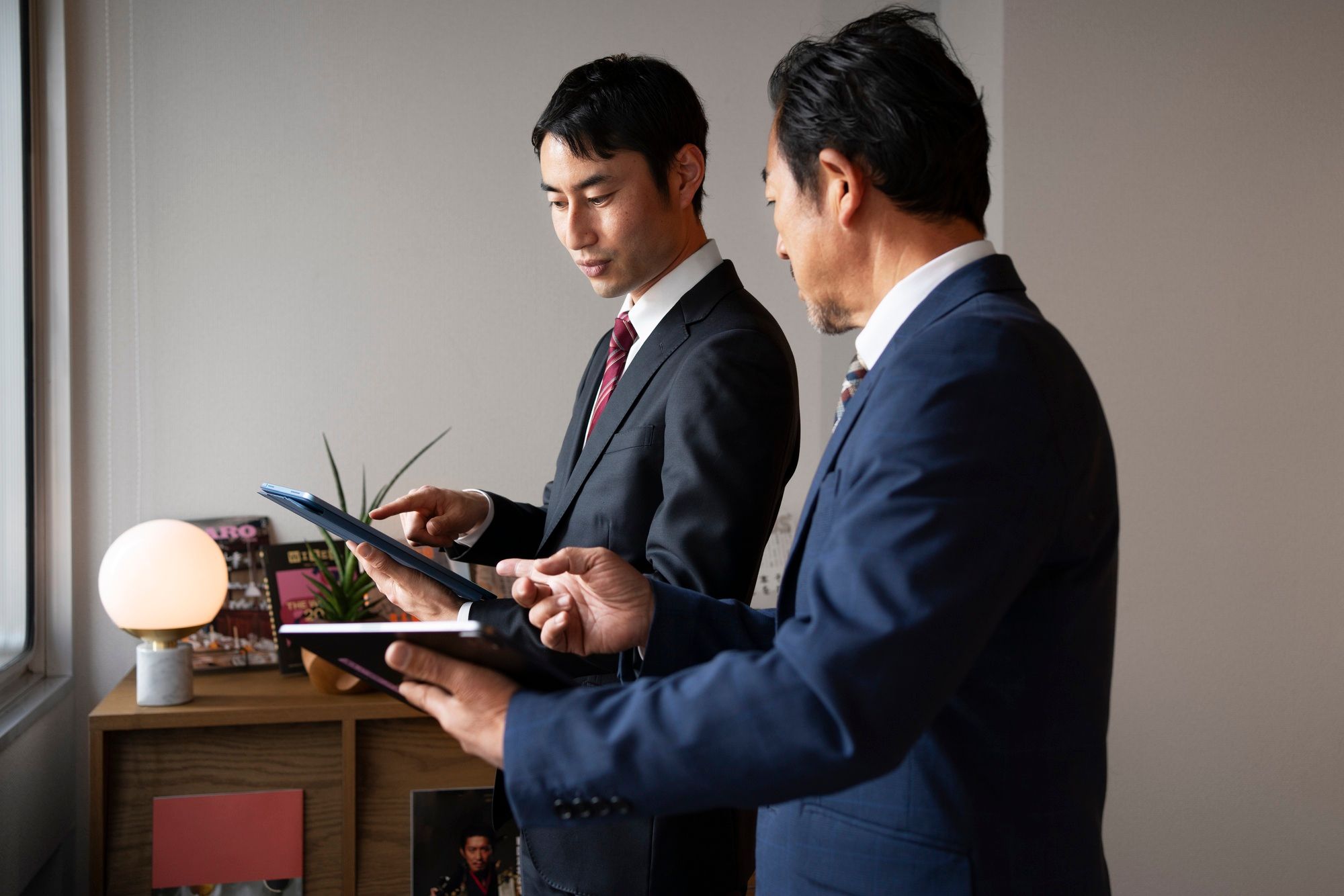 Two businessmen in suits discussing work while using tablets.
