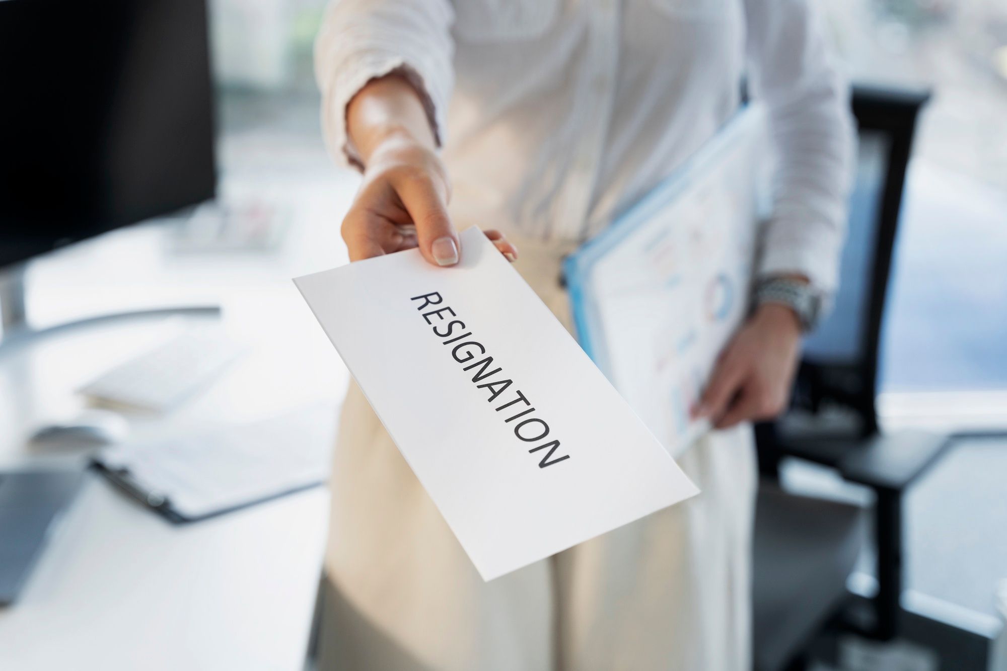 Close-up of a person handing over a formal document or resignation letter while standing in an office setting.