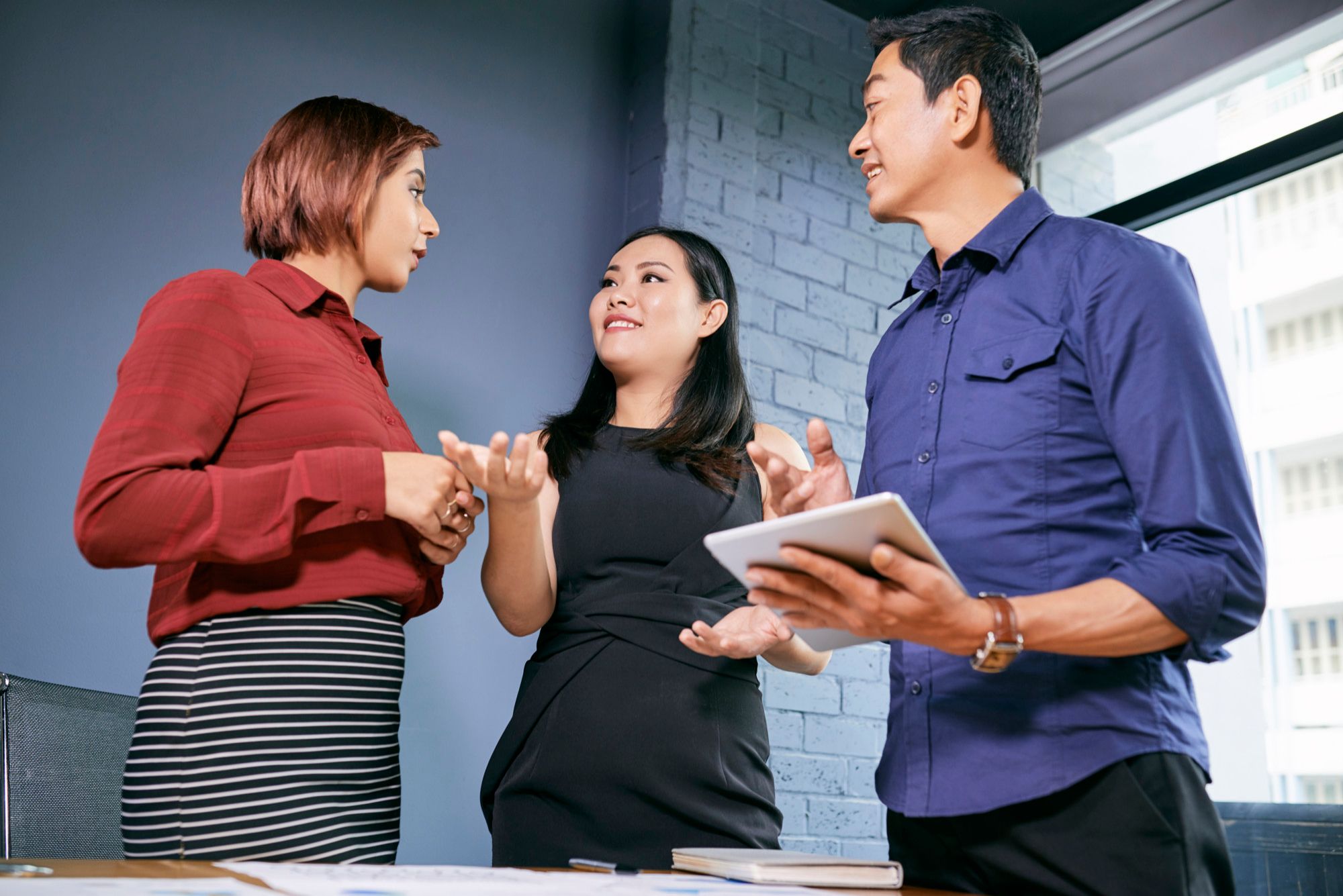 Three professionals having a lively discussion in an office, exchanging catchy tagline examples to enhance branding and communication strategies.