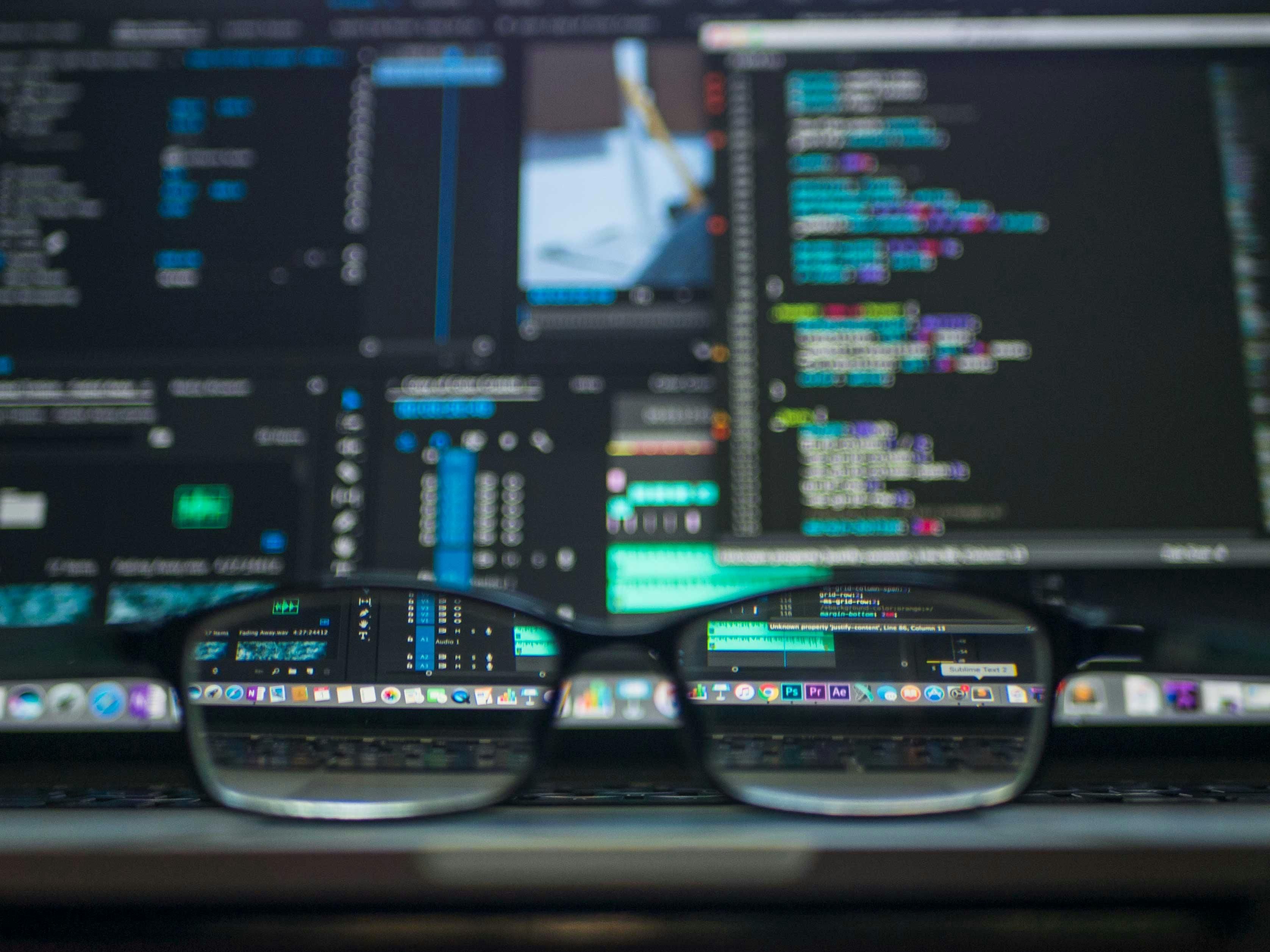A laptop screen displaying code, viewed through a pair of eyeglasses in the foreground.