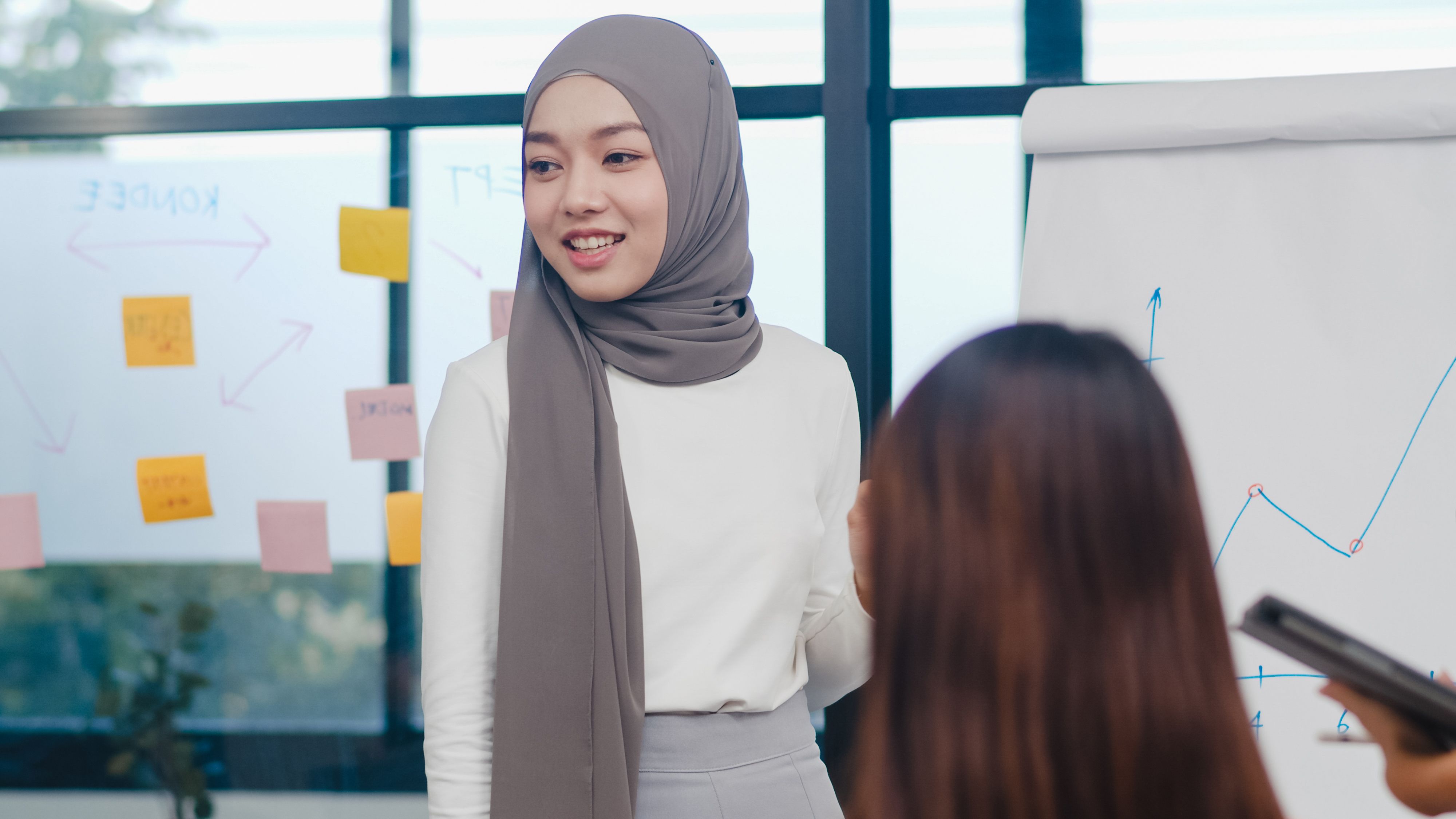 Seorang perempuan bertudung sedang melakukan pembentangan di pejabat.