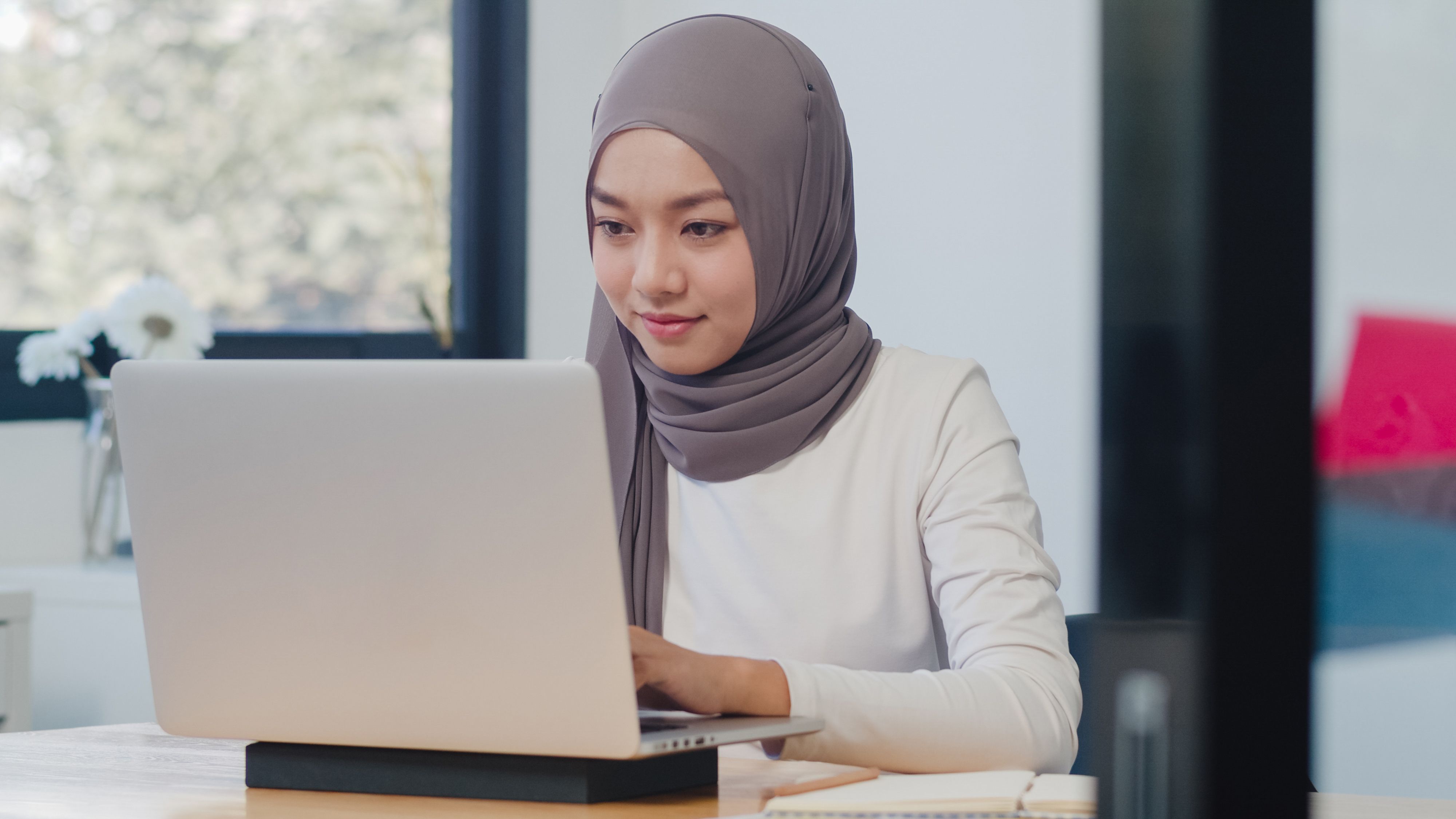 Seorang perempuan bertudung sedang menggunakan komputer riba.