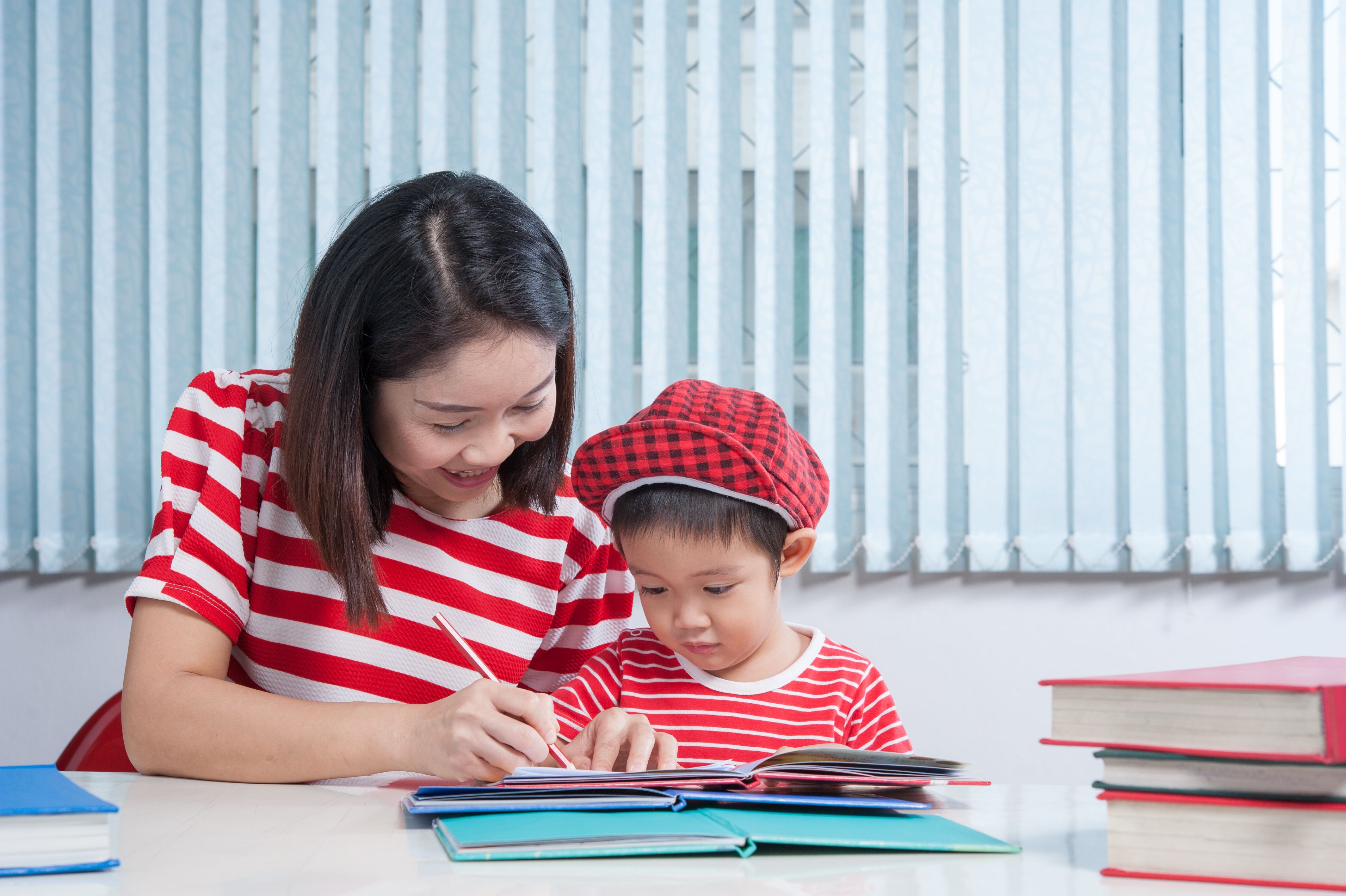 Cute boy doing his schoolwork with his teacher, at home, he is writing on a book