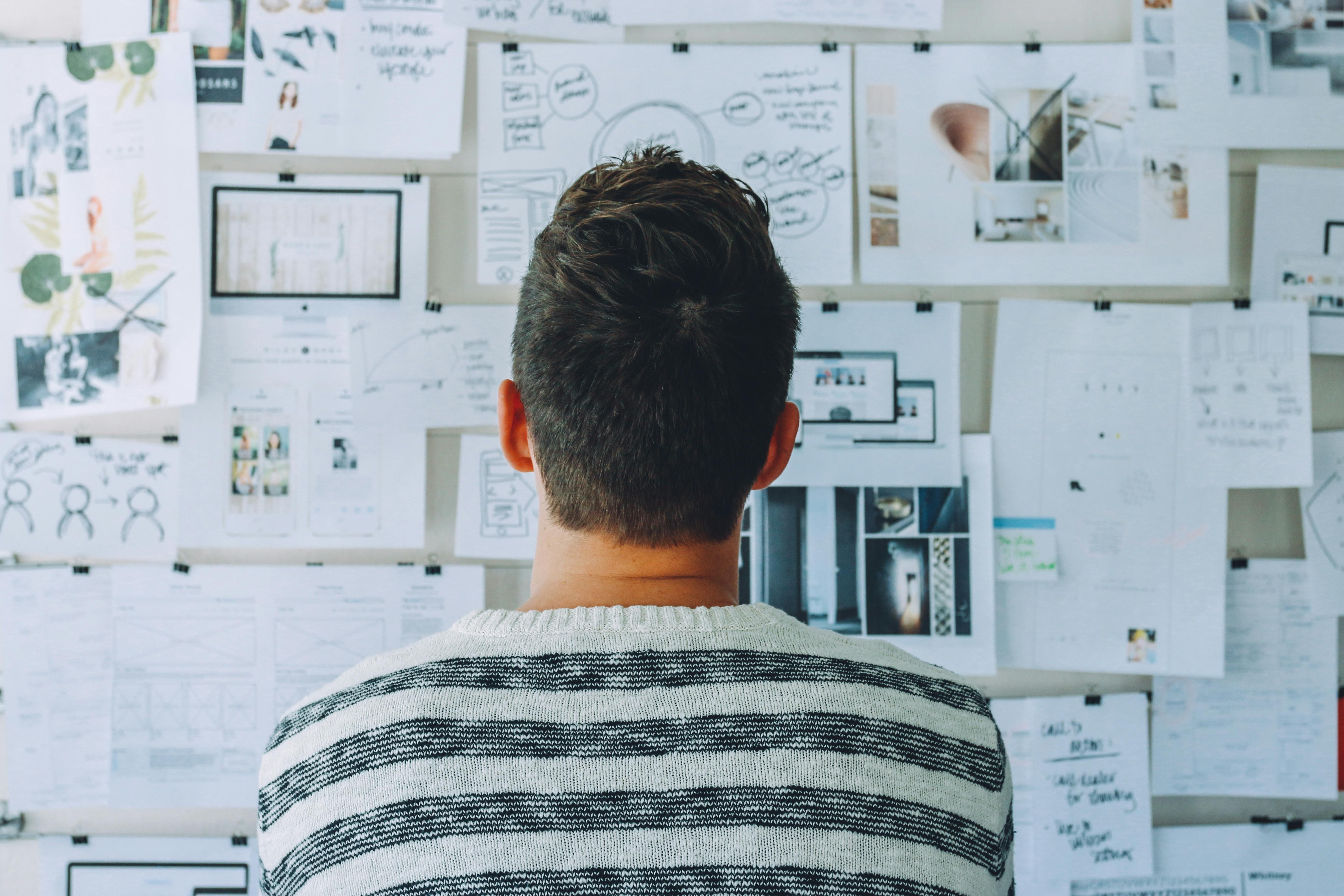 Man looking at board covered with papers and diagrams, trying to solve a problem.