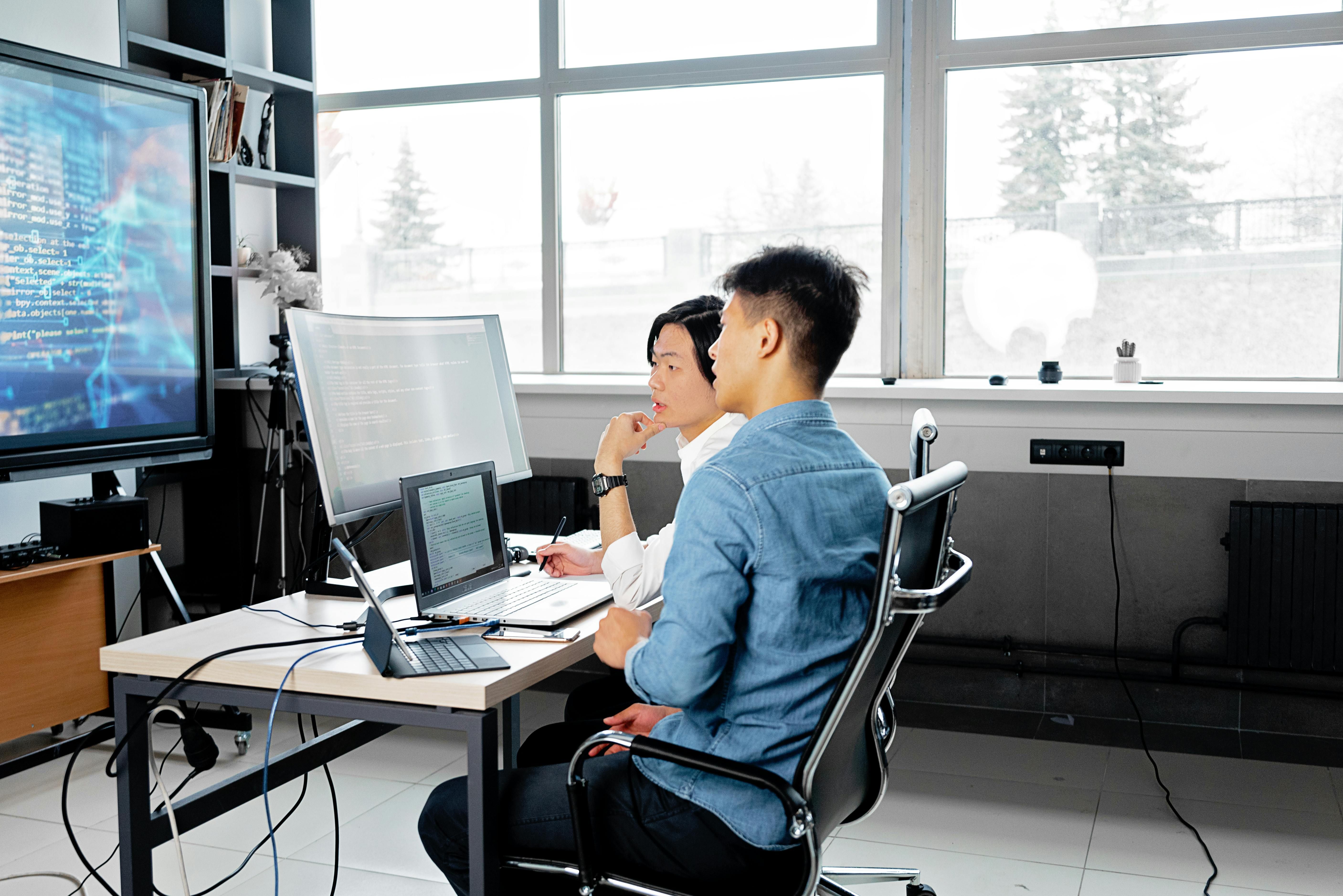 Two professionals discussing code in a modern office, highlighting digital skills and management in tech.