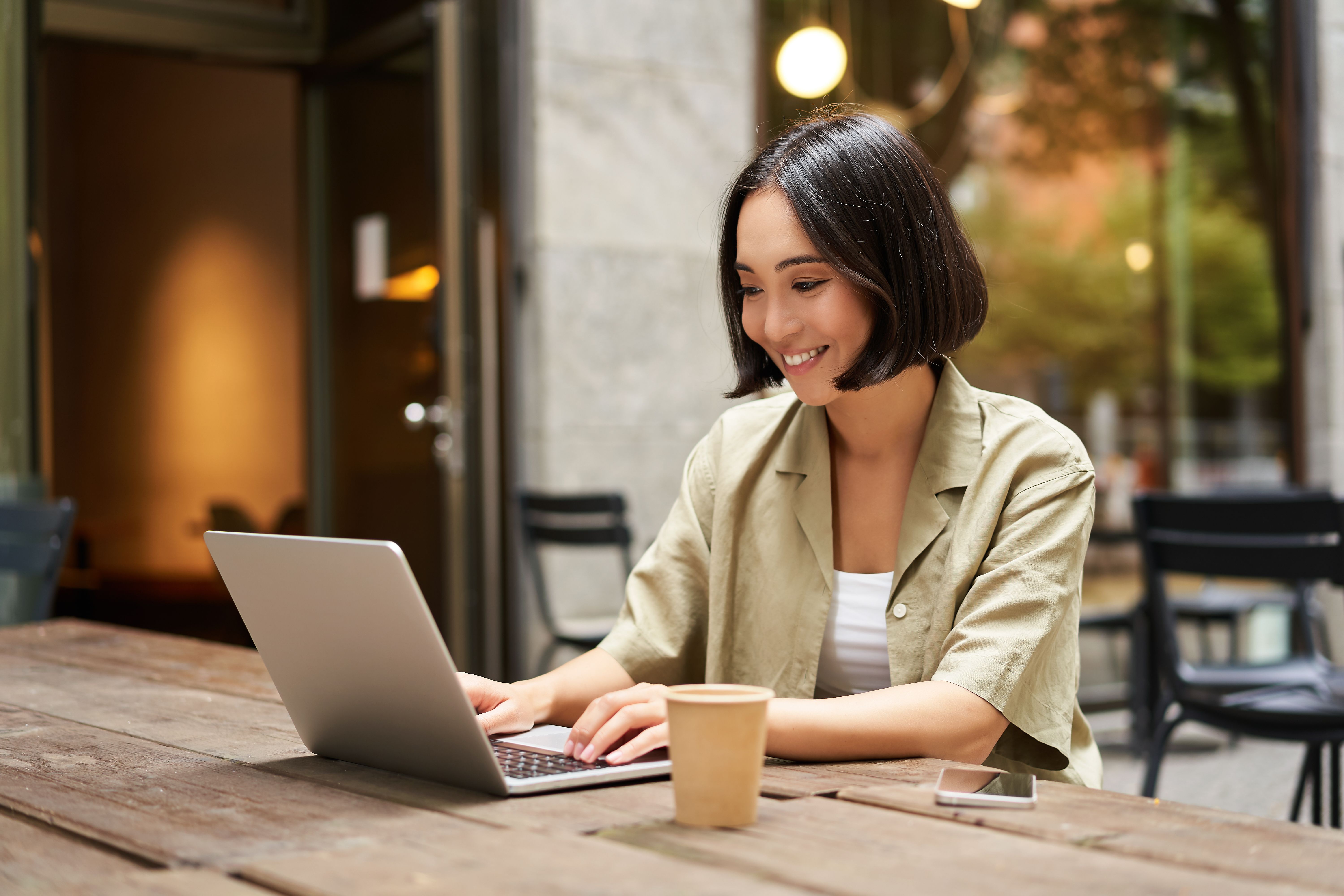 Young Asian woman smiling while typing on her laptop