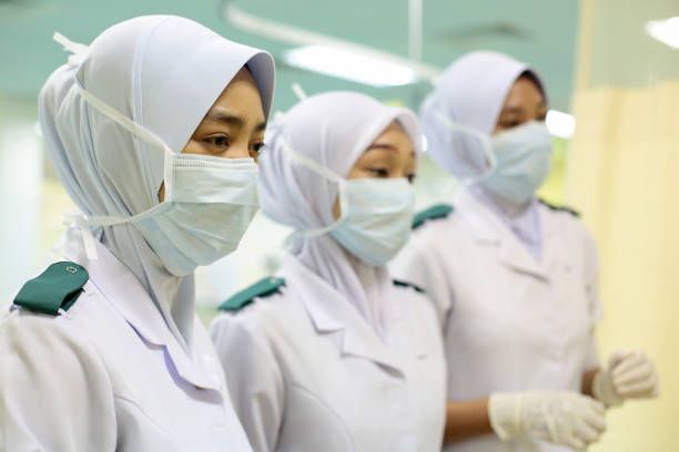 Tiga orang jururawat memakai topeng muka dan bersedia untuk bertugas di hospital. 