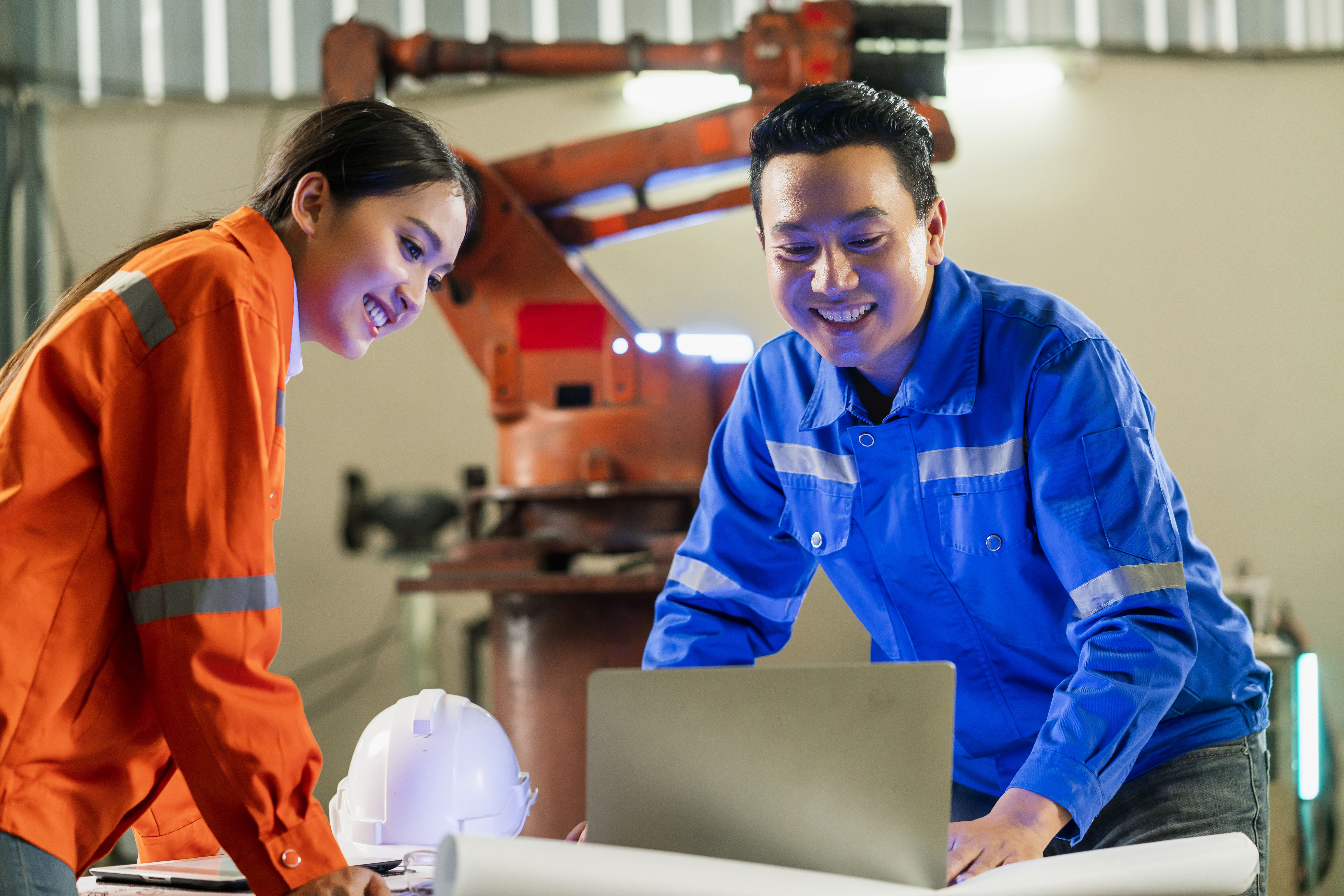 Two engineers collaborating in a smart manufacturing facility, reviewing plans and discussing technical roles, which will be included in their next curriculum vitae.