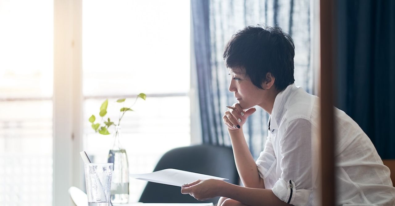 An Asian woman in a white shirt sitting and thinking about her career